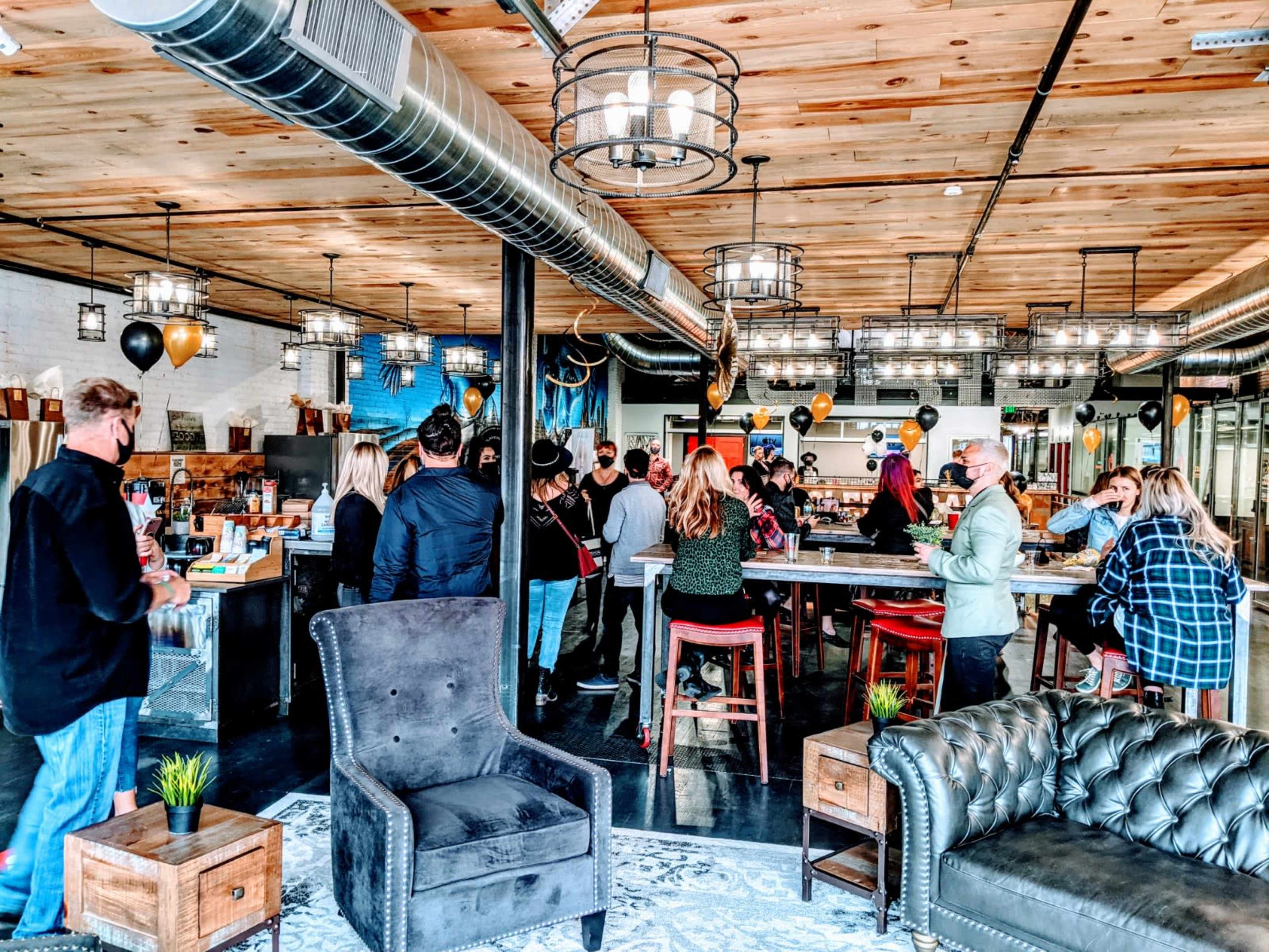 A group of people gathers around a large bar area in a modern, open space decorated with balloons and wooden accents.