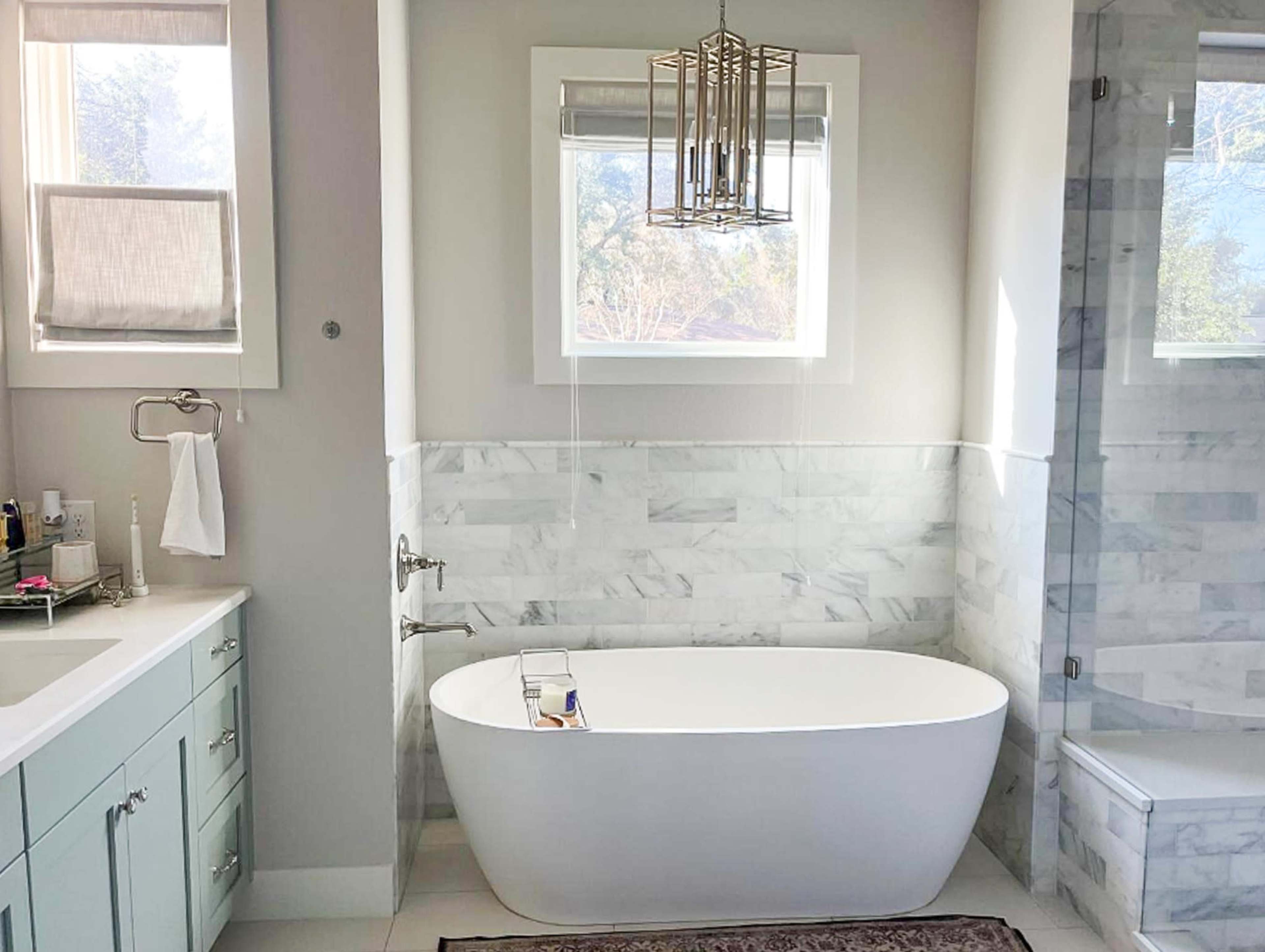 A modern bathroom featuring a freestanding white bathtub, light gray walls, and marble accents.