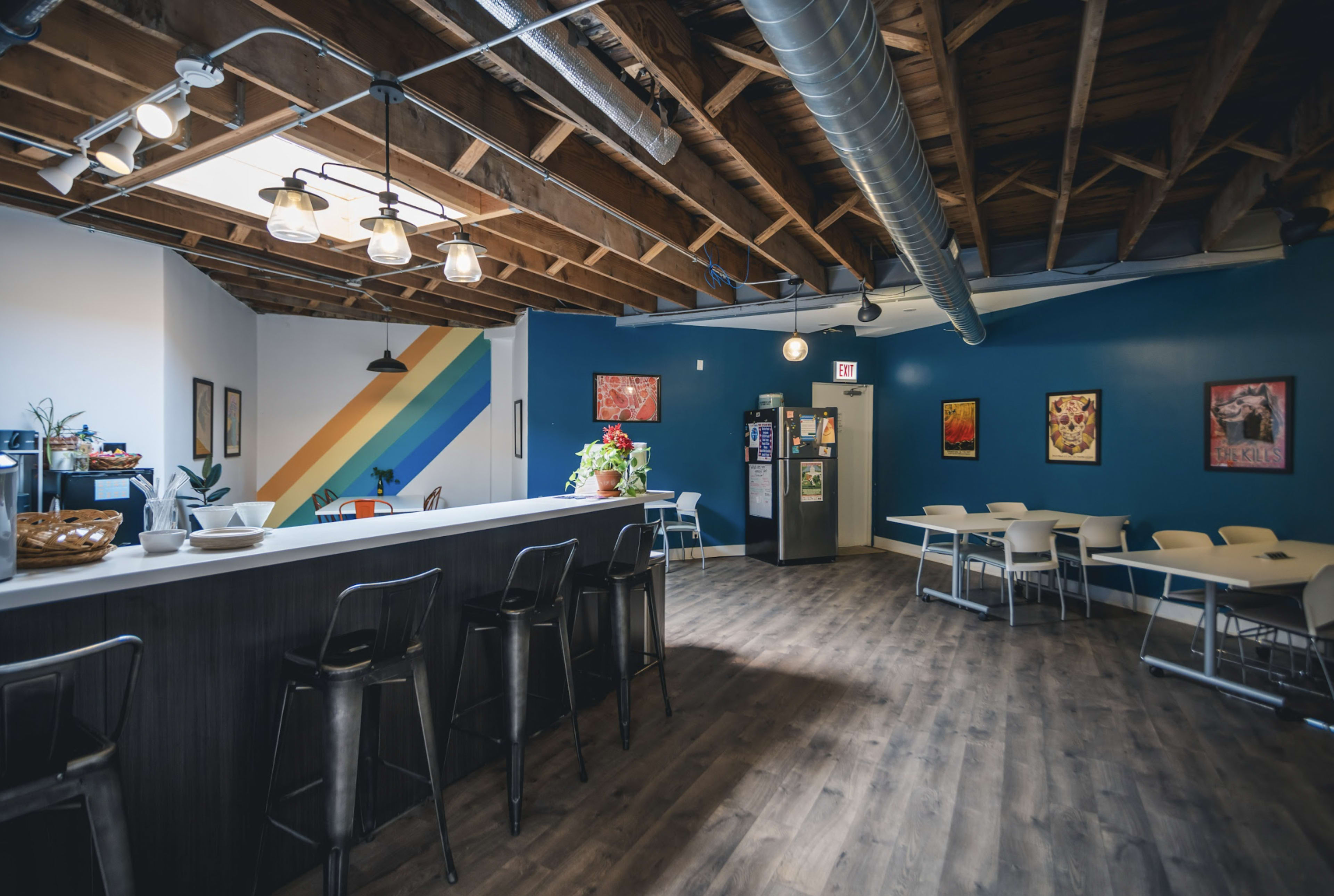 A modern café interior with a bar area, seating tables, colorful wall art, and a skylight.