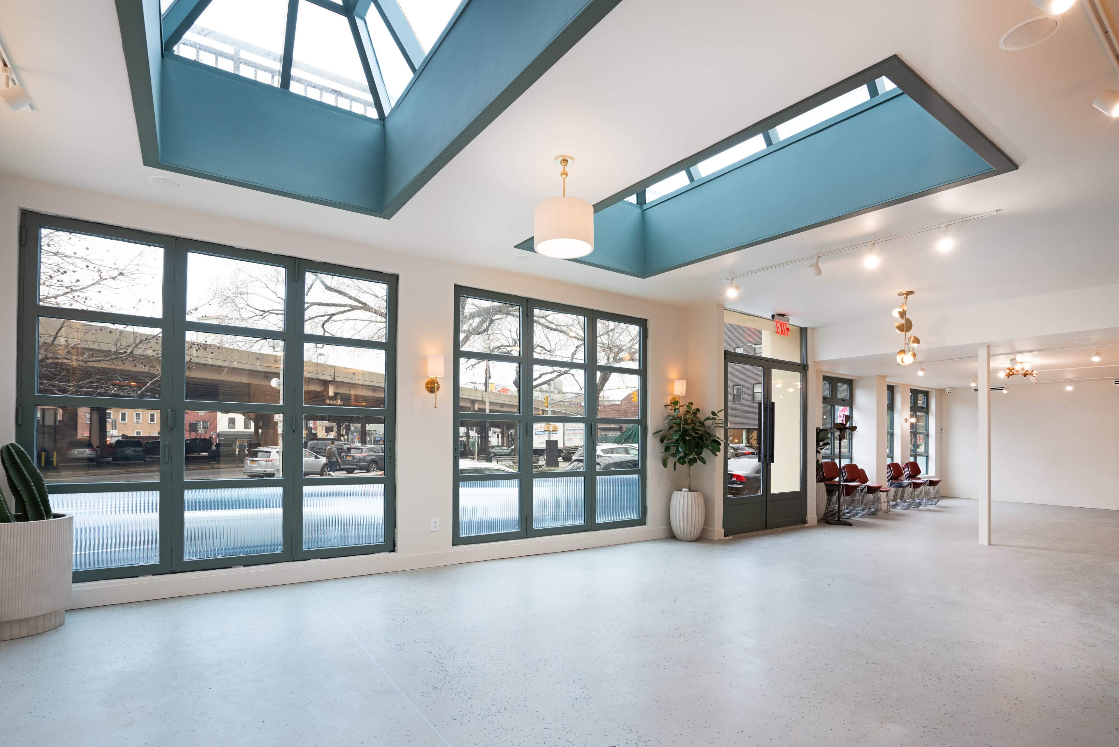 A bright, open interior space with large windows, skylights, and a view of an urban street outside.