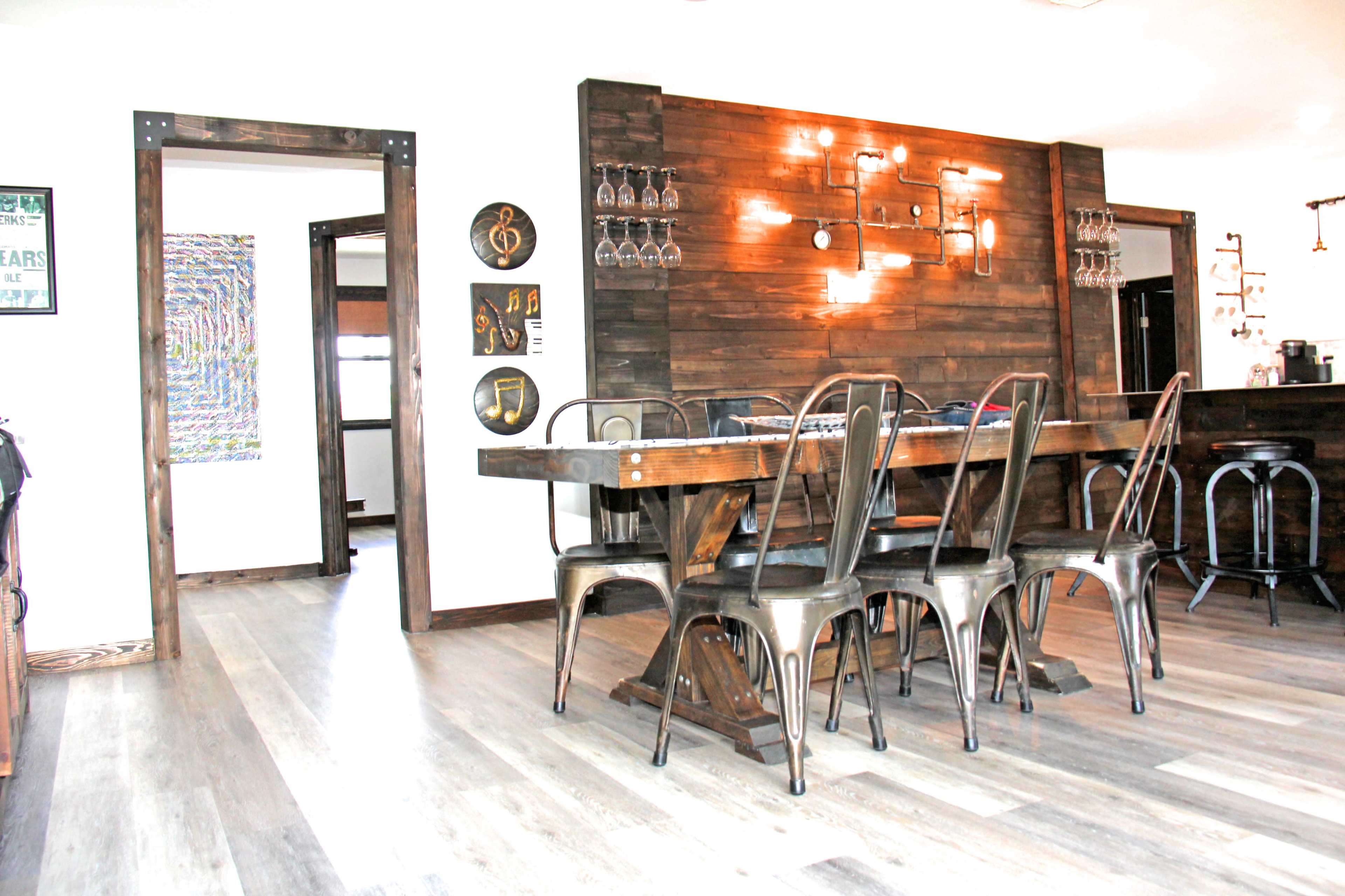 A modern dining area featuring a wooden table surrounded by metal chairs, with a rustic accent wall and various decorations.