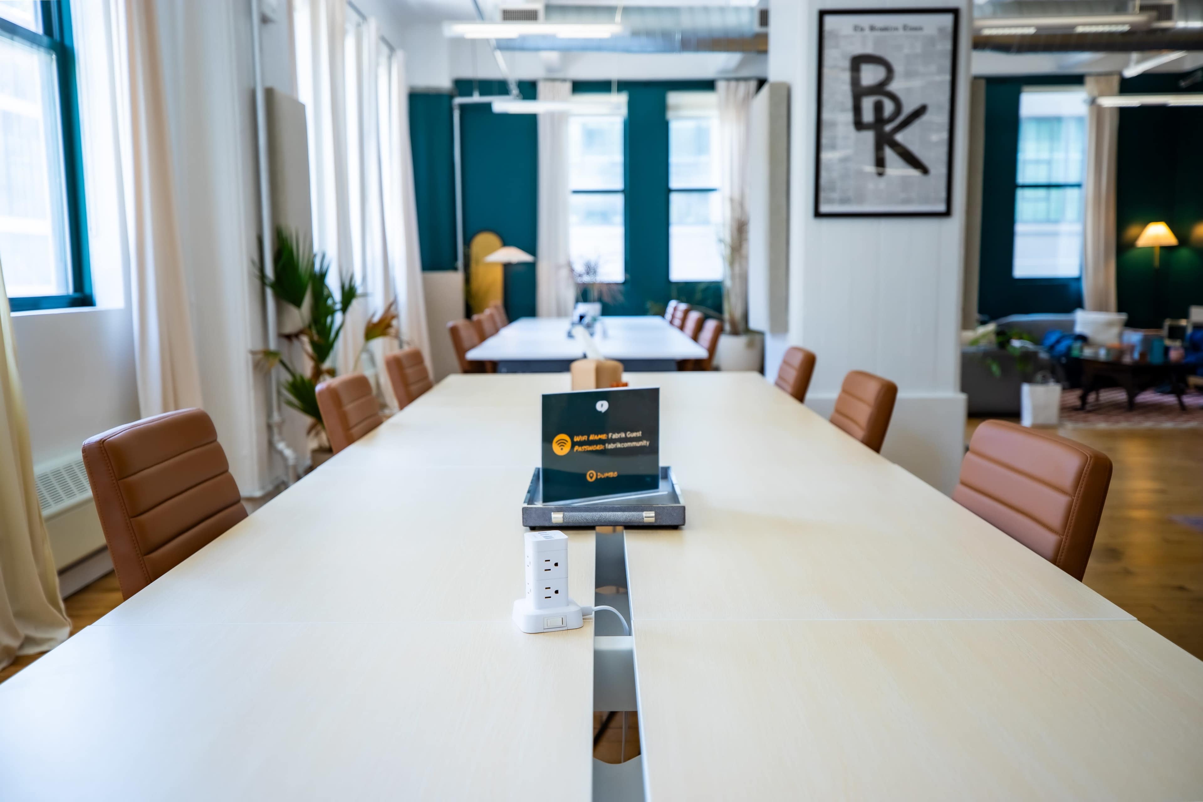 The image shows a modern conference room with a long wooden table, leather chairs, and a display stand in the center.