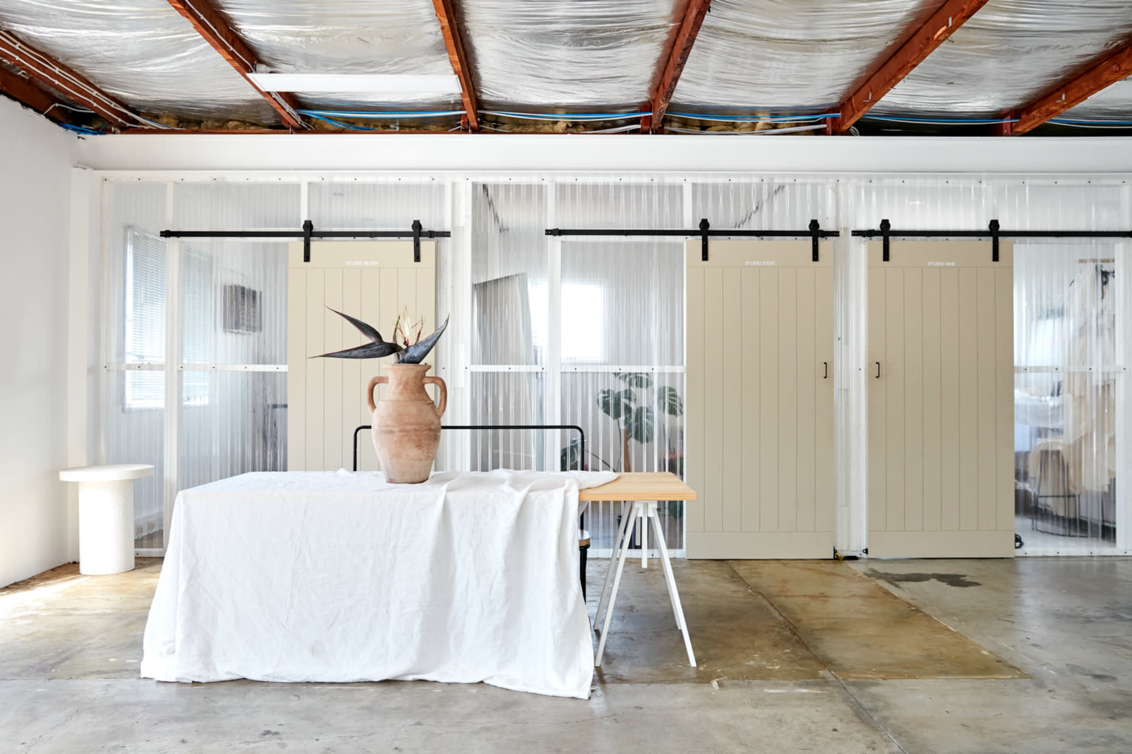 A spacious interior with a table covered by a white cloth, a ceramic vase on top, and two sliding barn doors in the background.