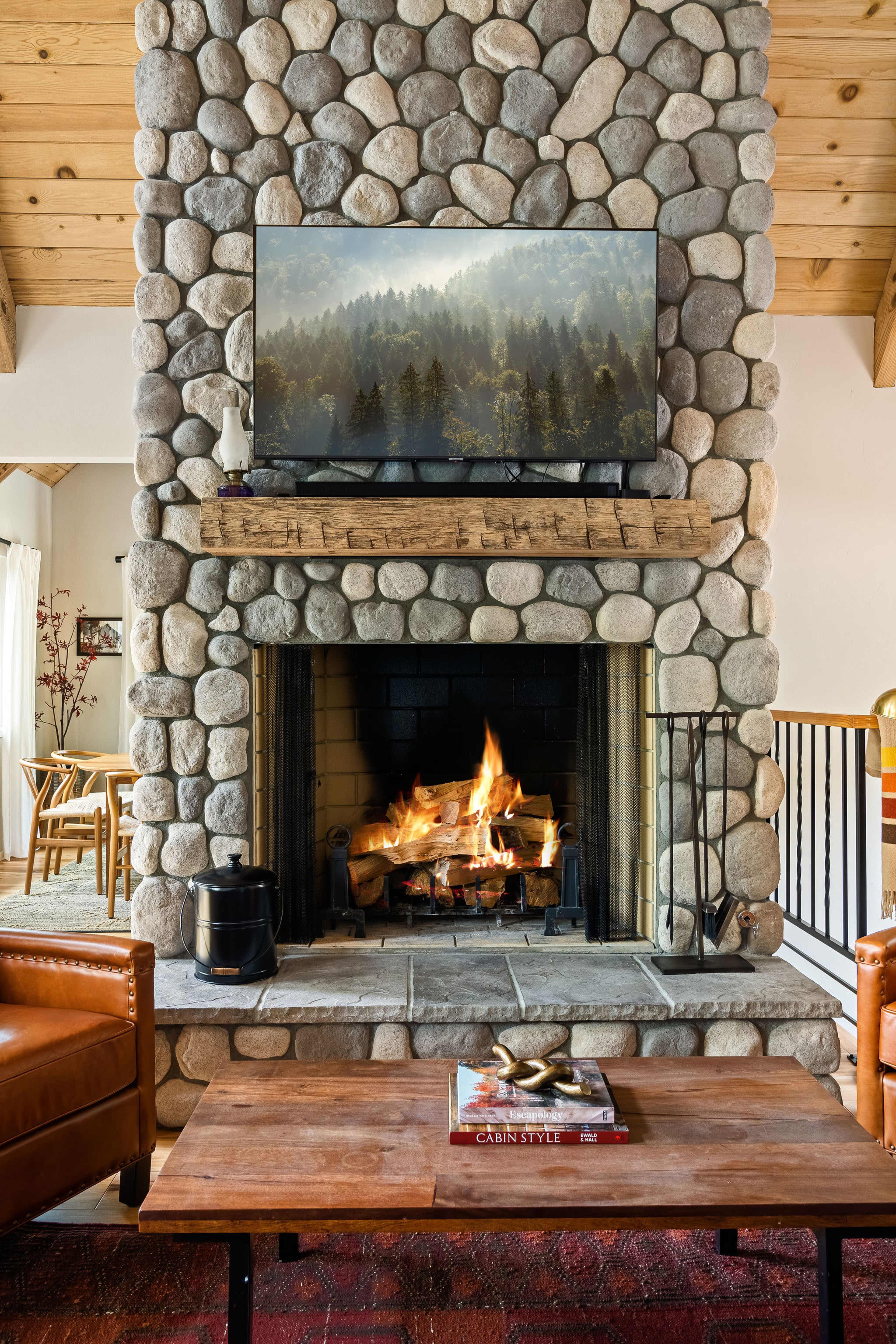 A stone fireplace with a television mounted above it, featuring a fire burning in the hearth and a wooden coffee table in front.