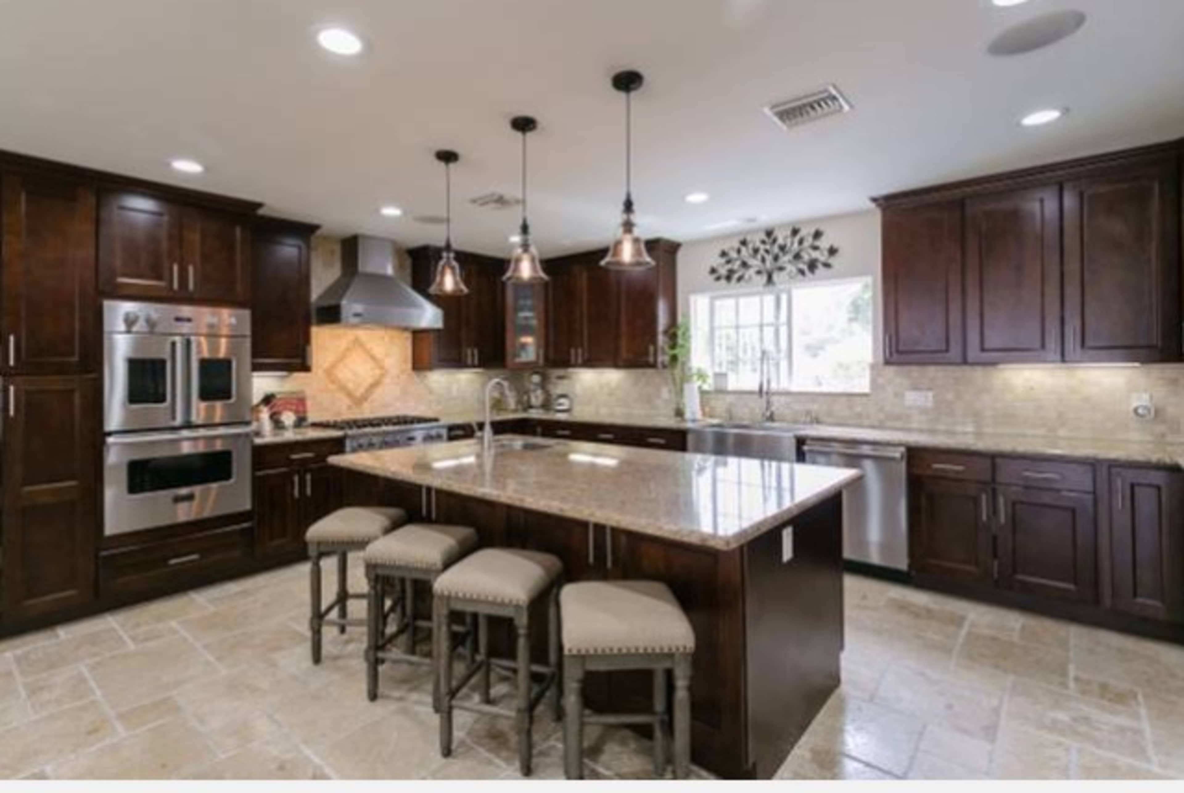 A modern kitchen features dark wood cabinets, stainless steel appliances, a central island with seating, and pendant lighting.