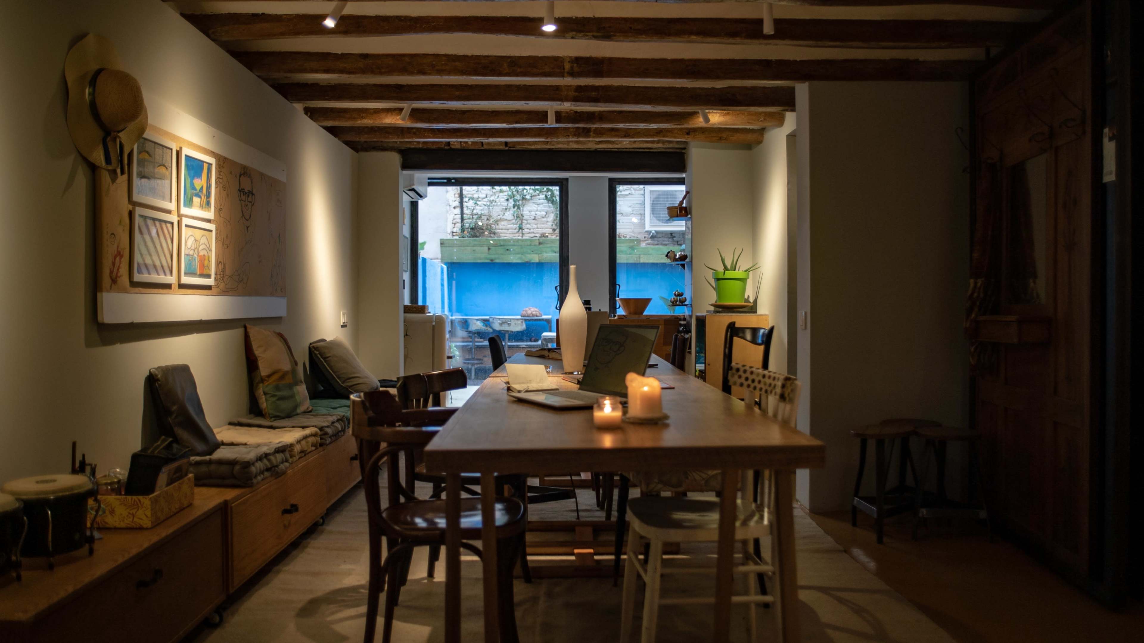 A cozy dining area with a long wooden table, surrounded by various chairs, and a view of a backyard through large glass doors.