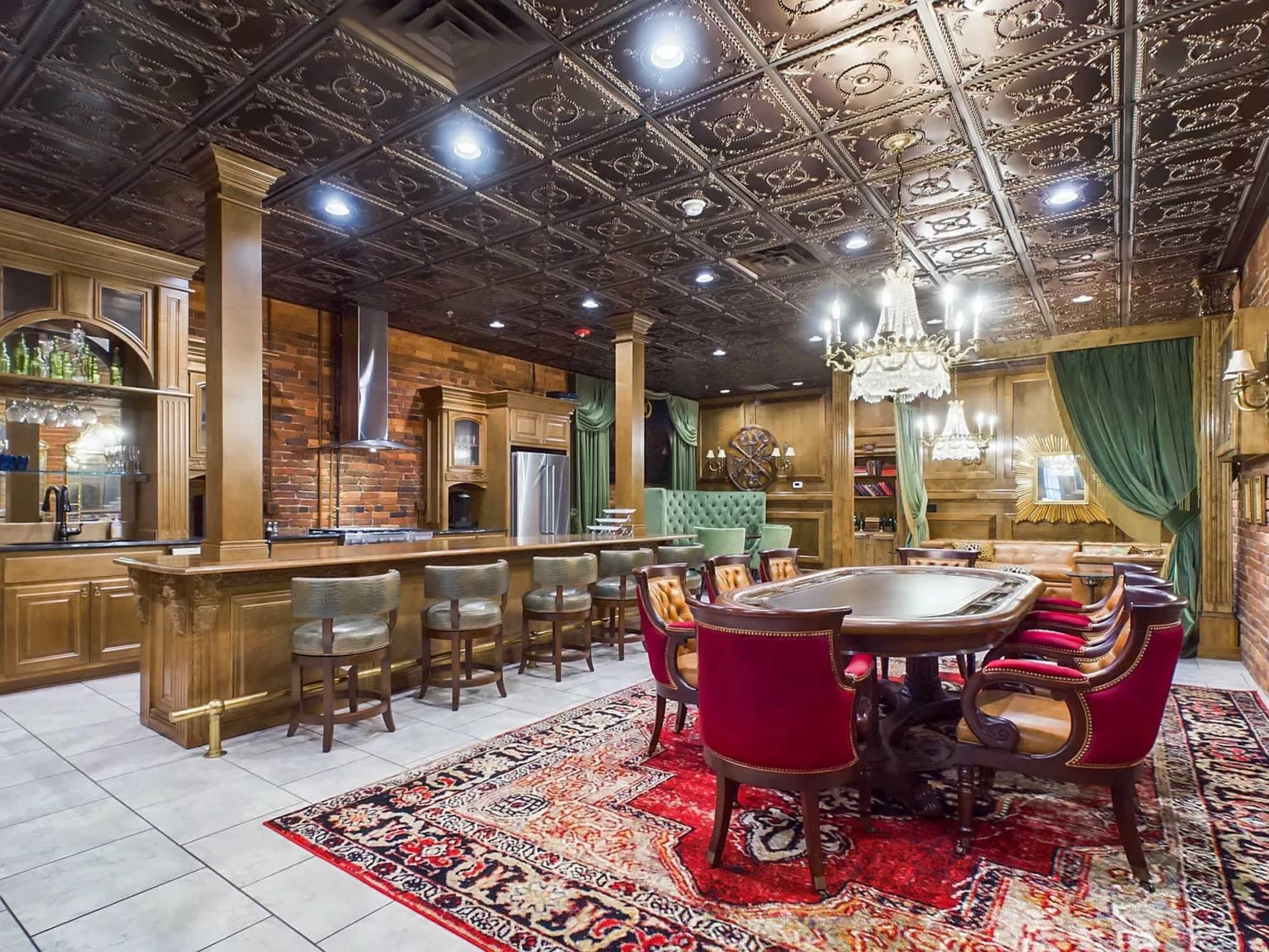 The image shows a well-furnished dining area with a large wooden table surrounded by upholstered chairs, a bar counter, and intricate ceiling details in a richly decorated interior.