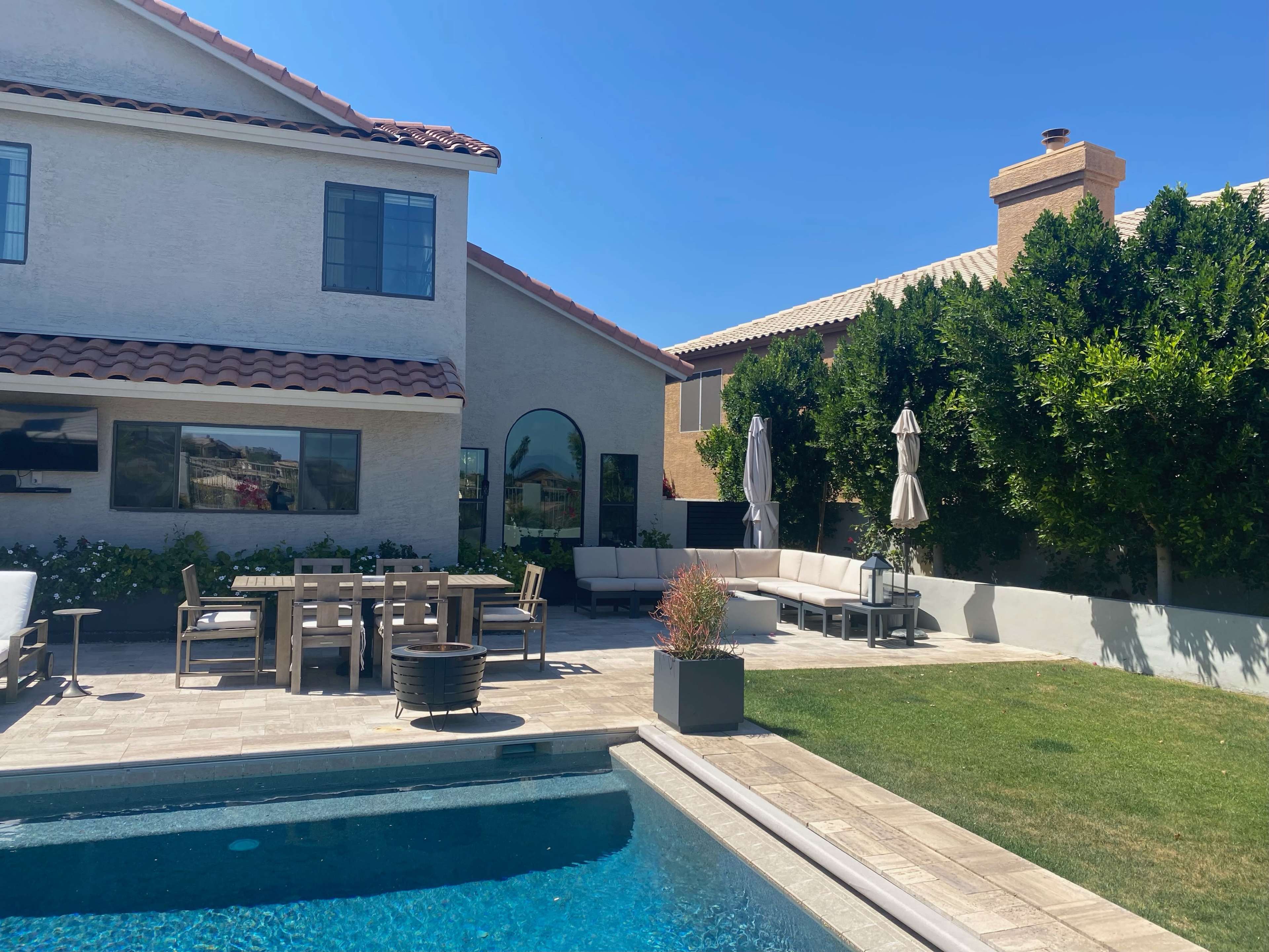 A backyard with a swimming pool, outdoor dining area, and a seating arrangement next to a landscaped garden.