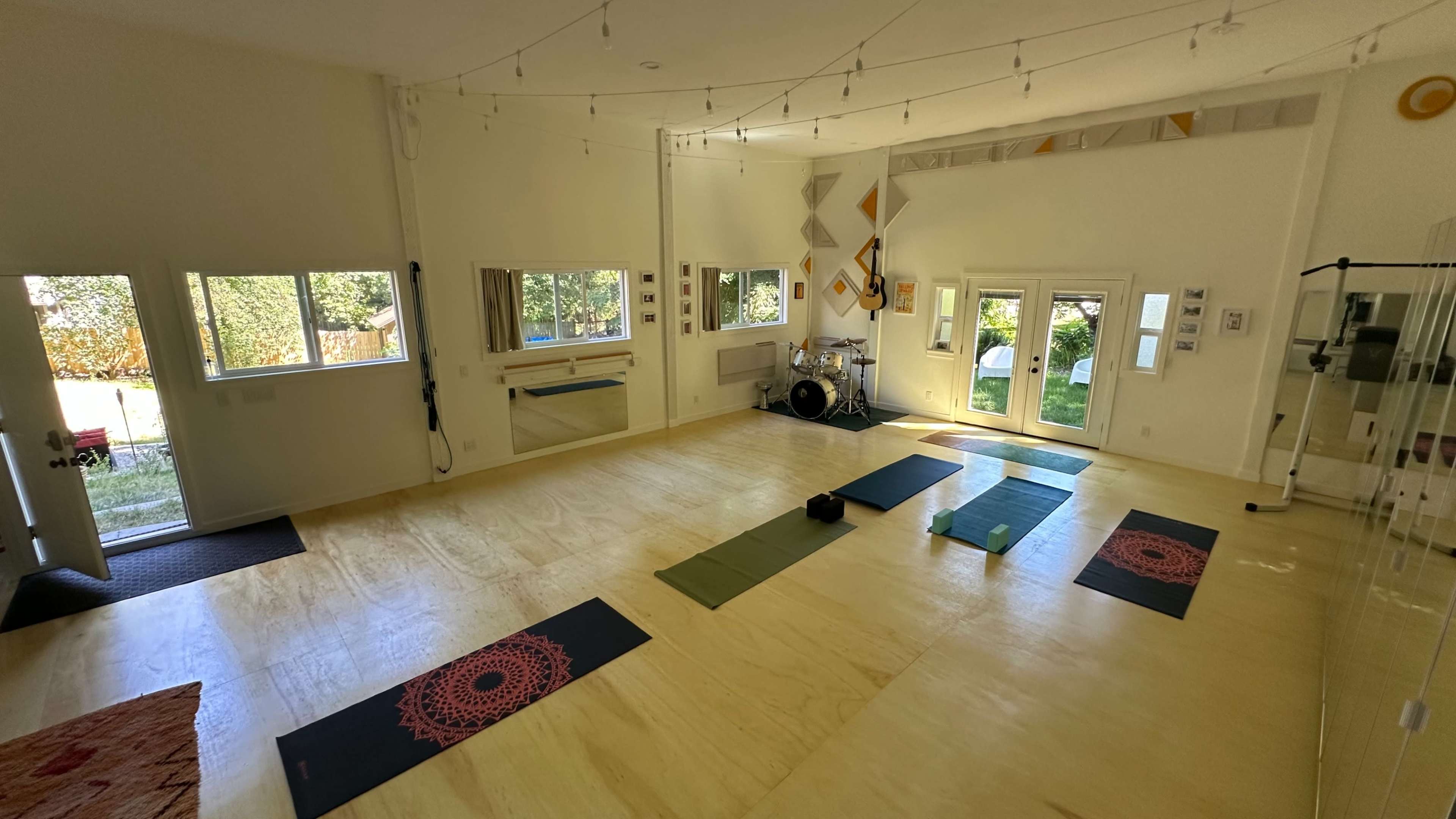 A spacious yoga studio features several mats arranged on a polished wooden floor, with large windows letting in natural light.