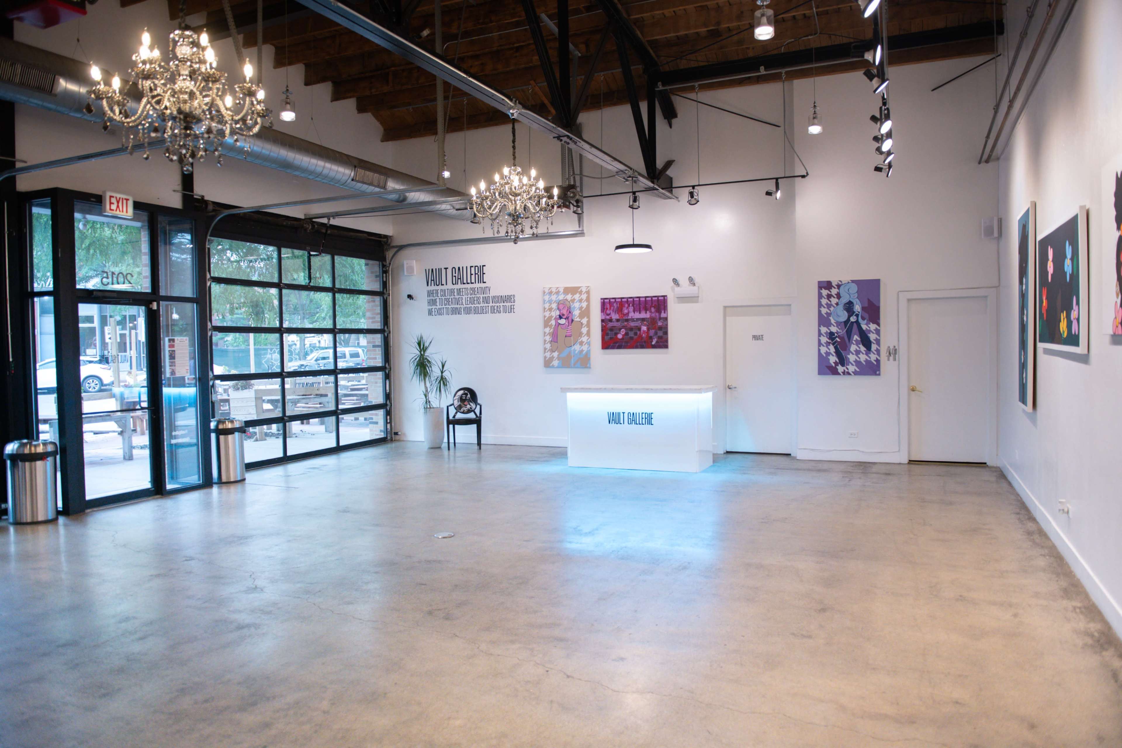 The image shows a spacious art gallery with polished concrete floors, elegant chandeliers, and various artworks displayed on the walls.