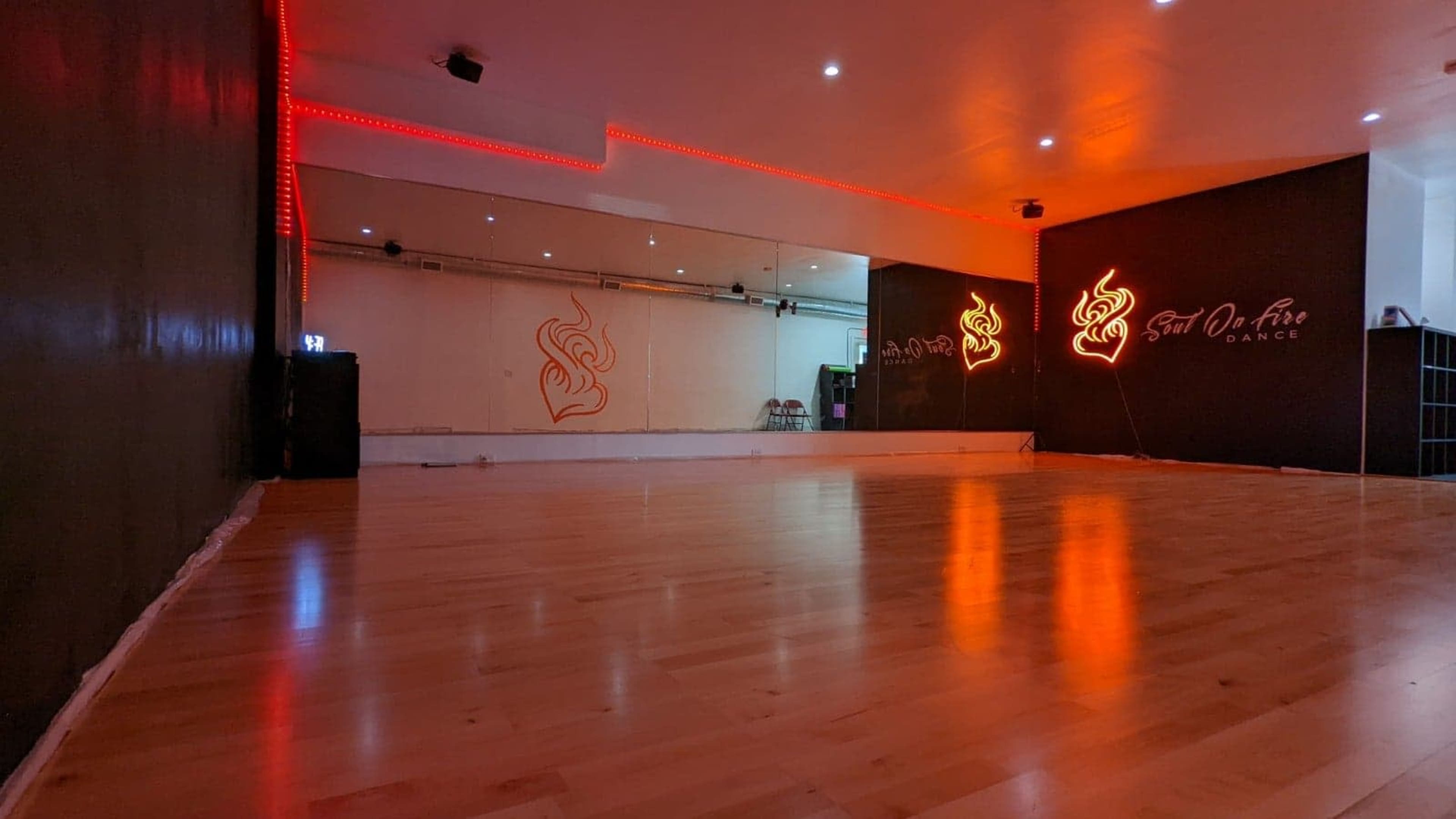 A dance studio with polished wooden floors, mirrored walls, and red lighting accents.