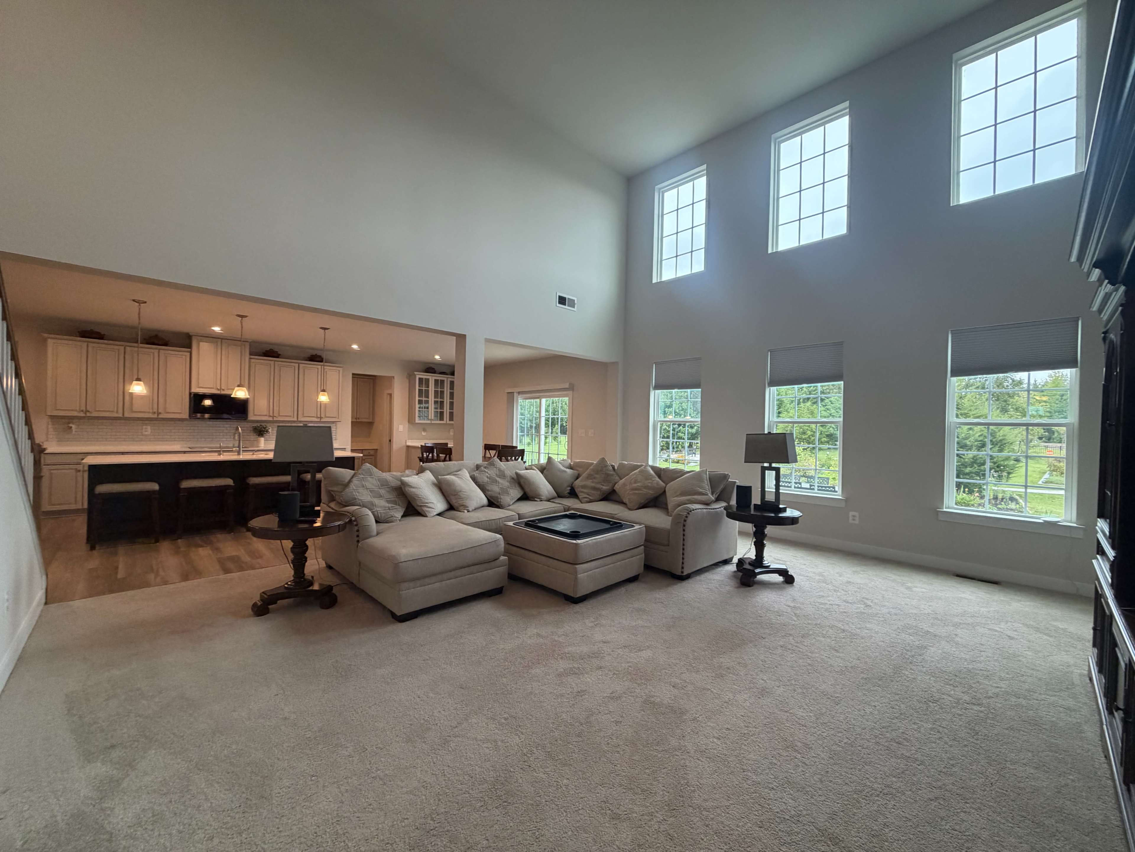 The image shows a spacious living room with a large sectional couch, a coffee table, and several windows allowing natural light to fill the area.