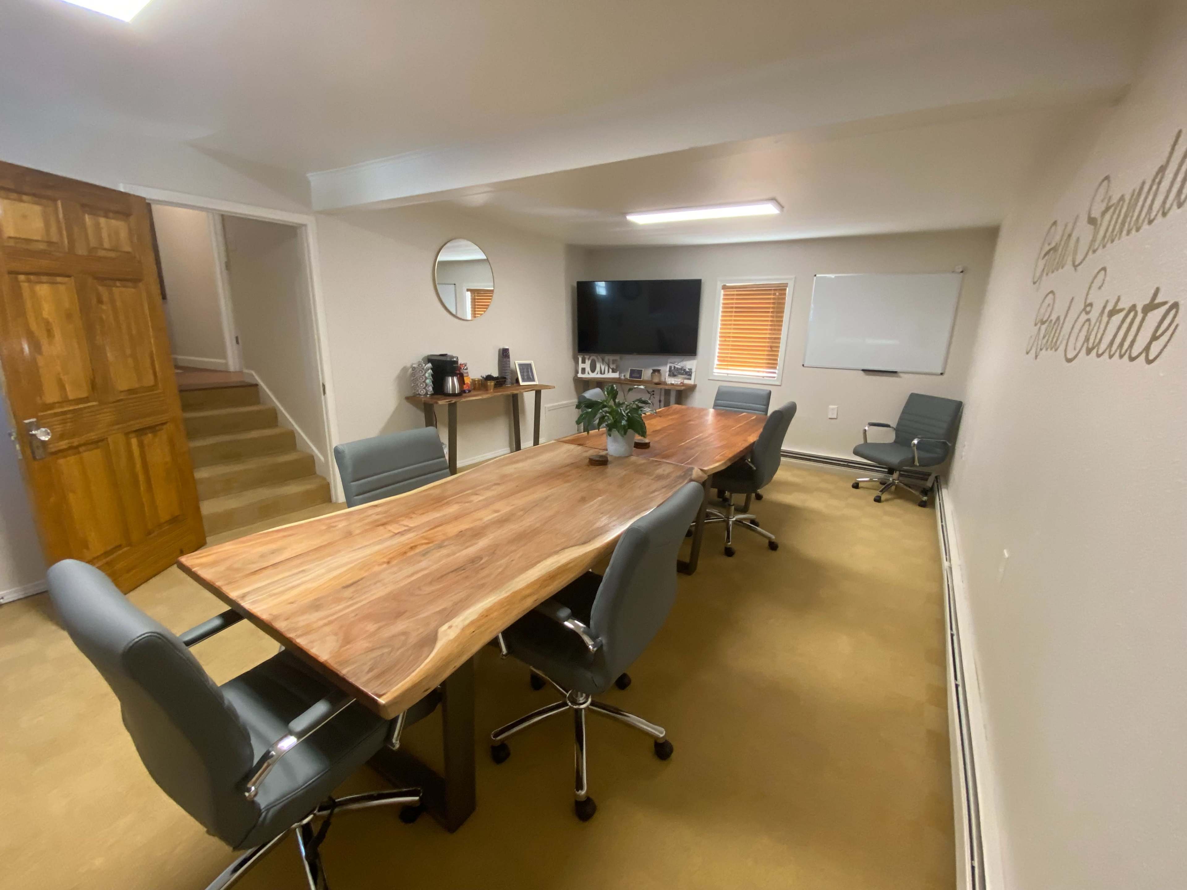 A conference room with a wooden table, gray office chairs, a television, and a whiteboard.