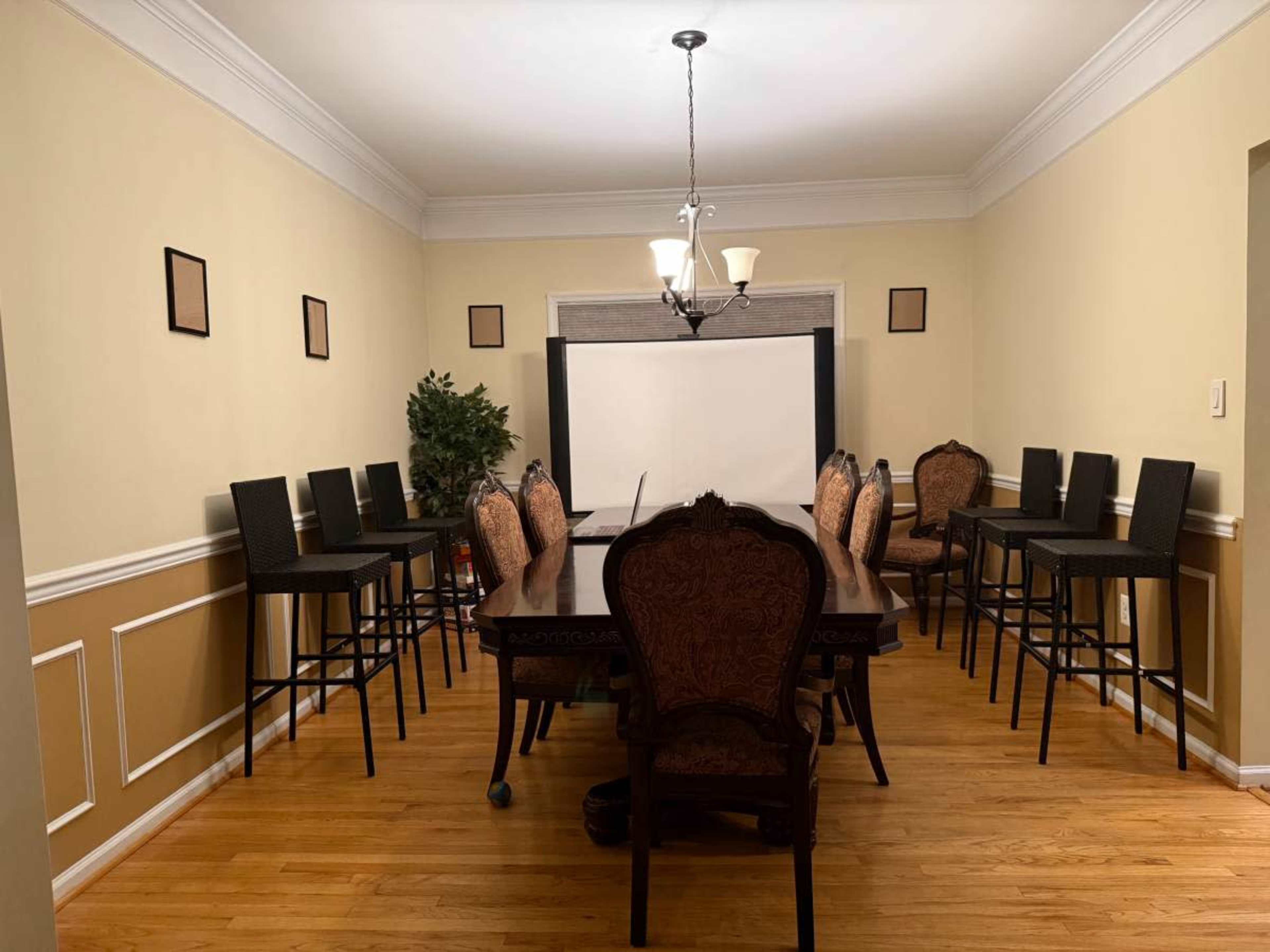 The image shows a dining room with a large table surrounded by chairs and several high stools positioned near the walls.