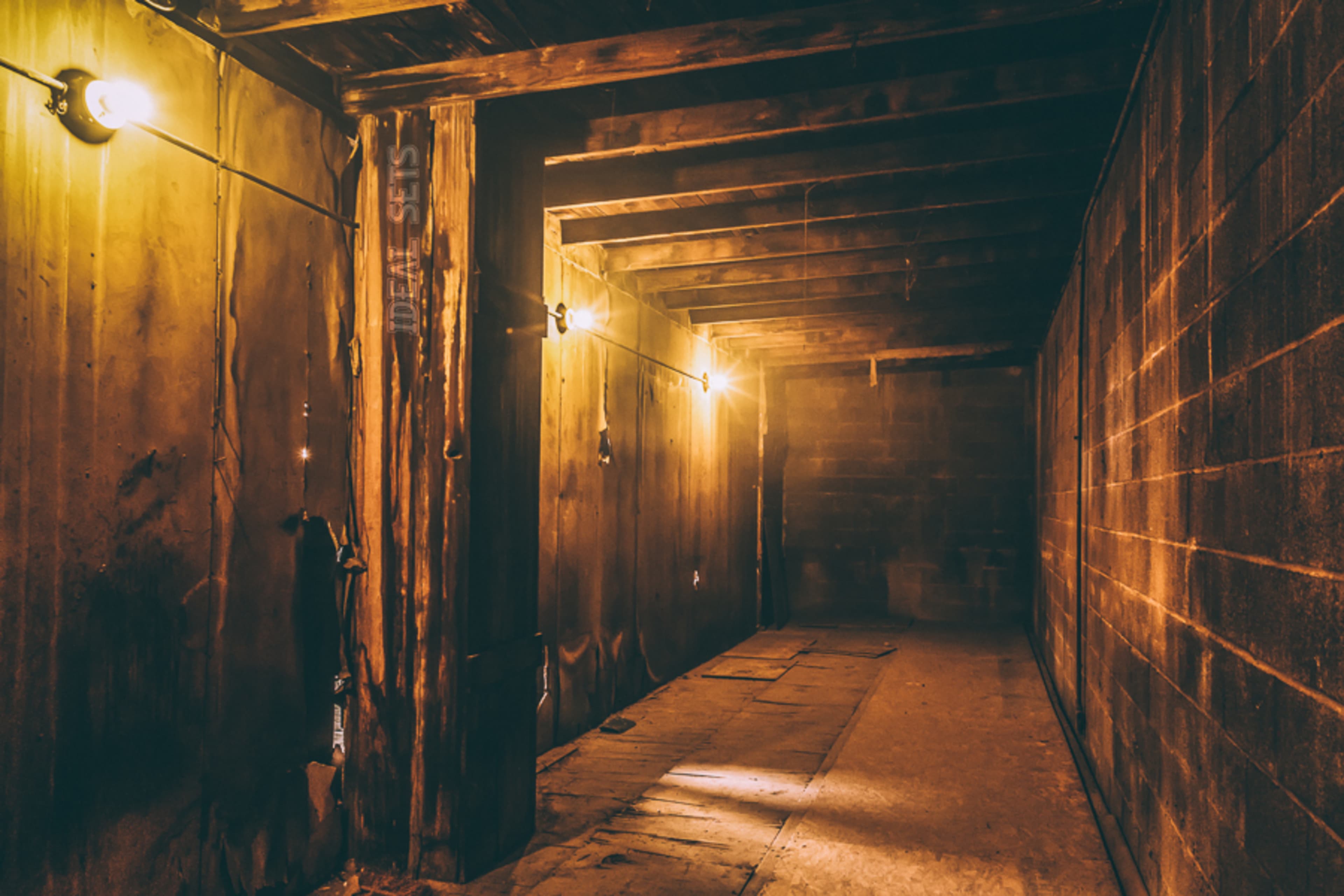 A dimly lit, narrow hallway with exposed wooden beams and concrete walls.