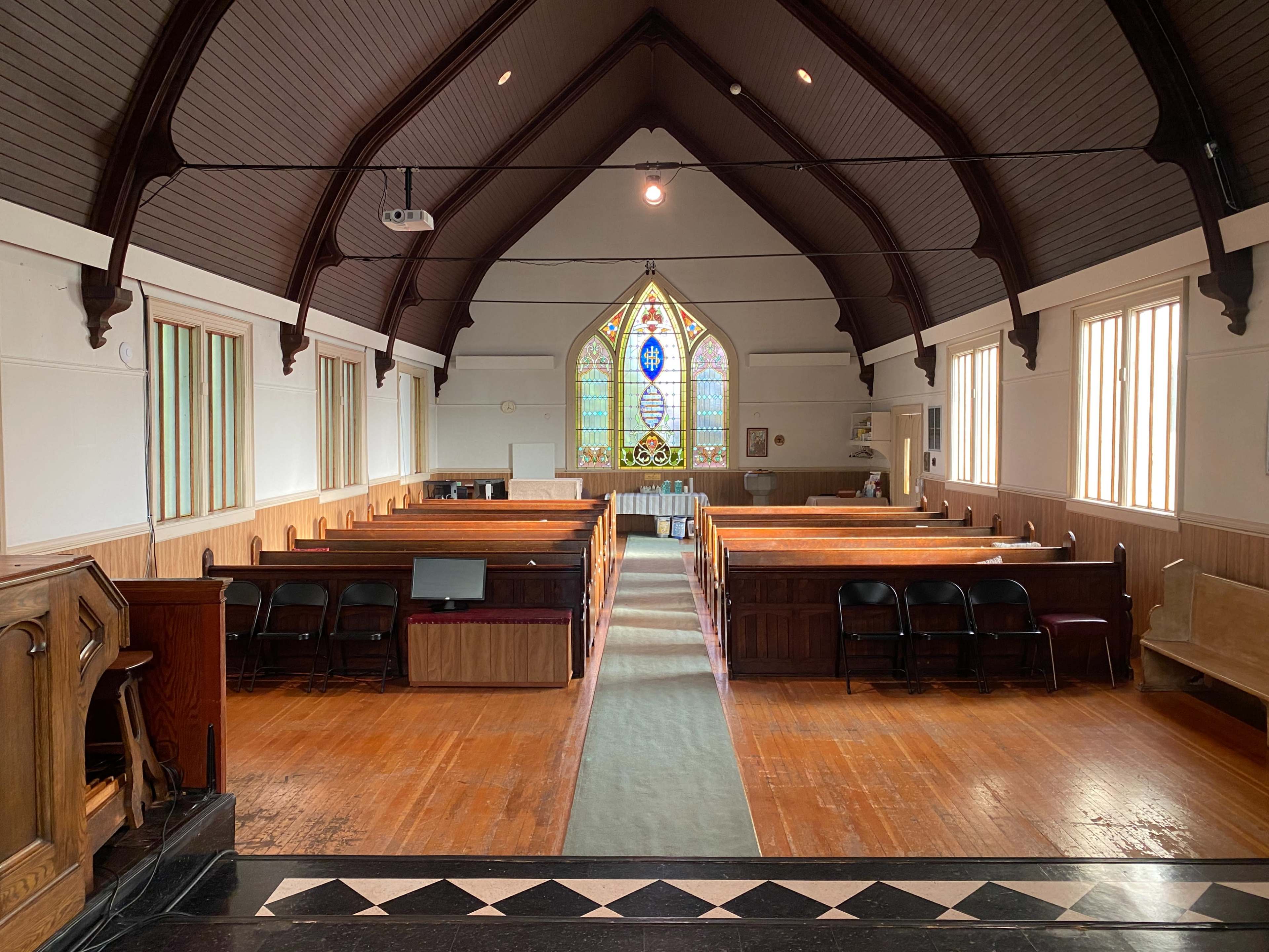 The interior of a church featuring wooden pews, a central aisle, and a stained glass window at the front.