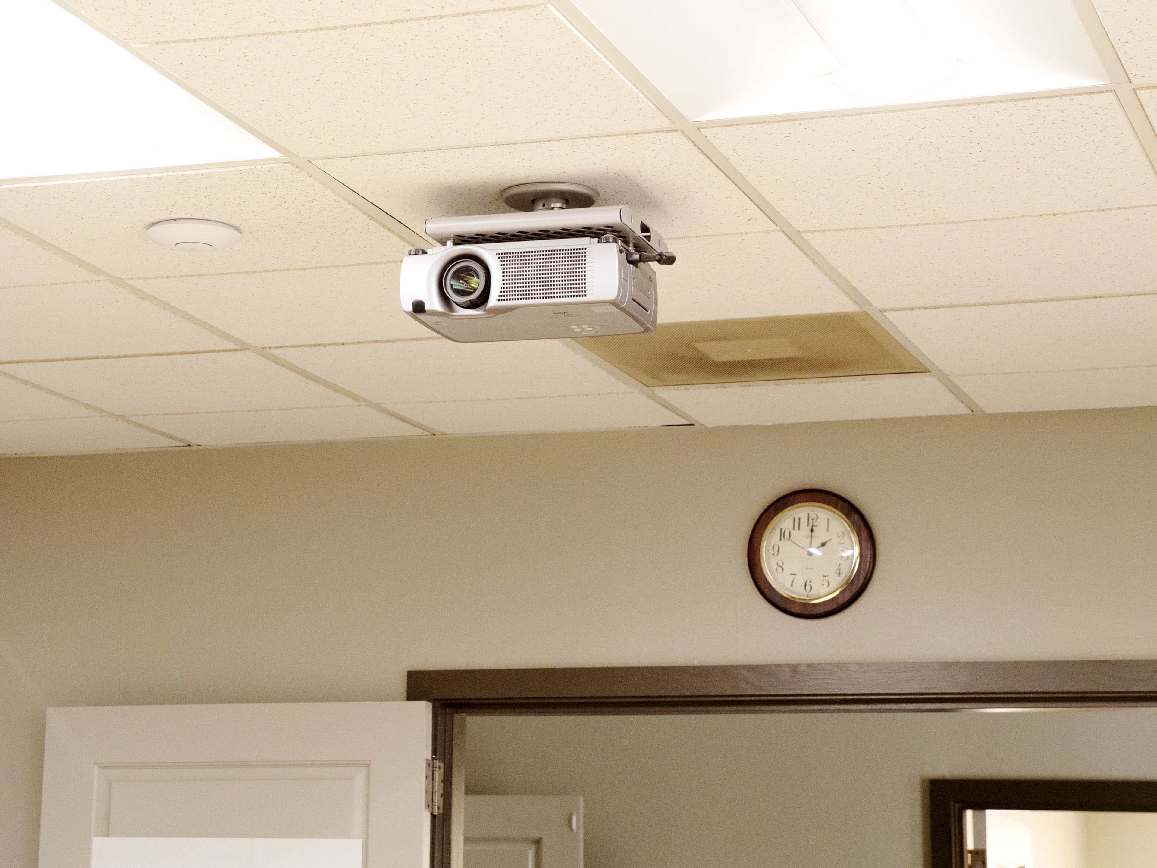 A ceiling-mounted projector is installed in a room with a clock on the wall.