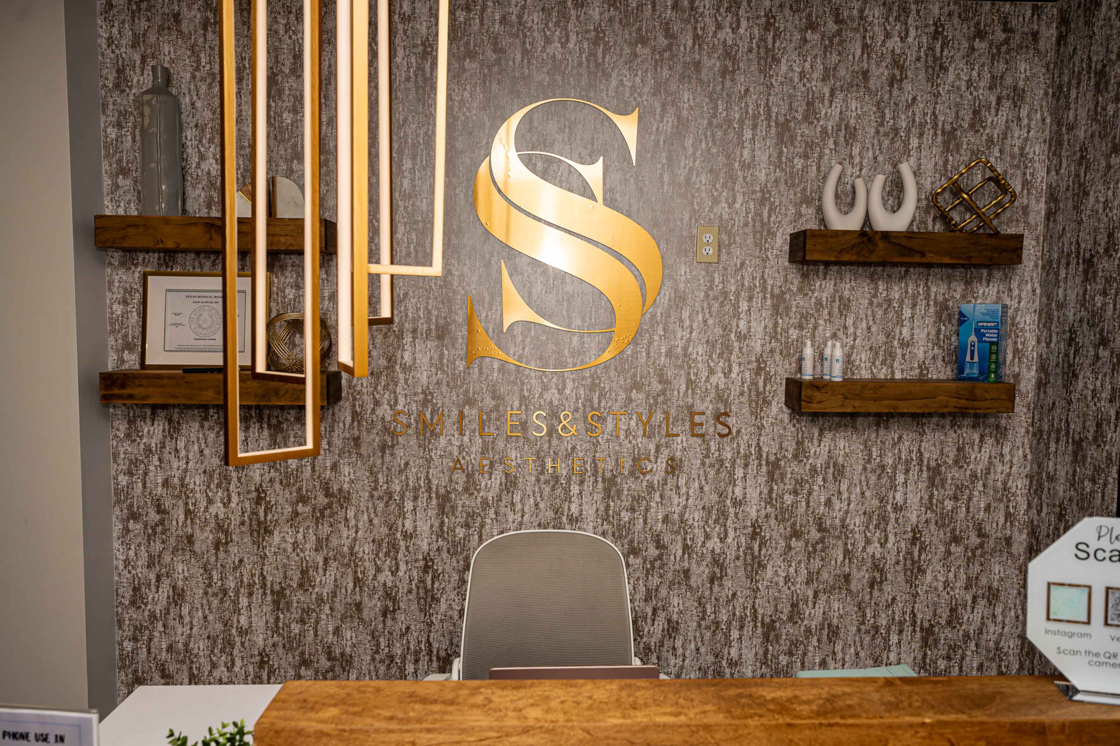 The image shows a reception area with a gold-lettered logo and the name "Smiles & Styles" on a textured wall, flanked by wooden shelves holding various items.
