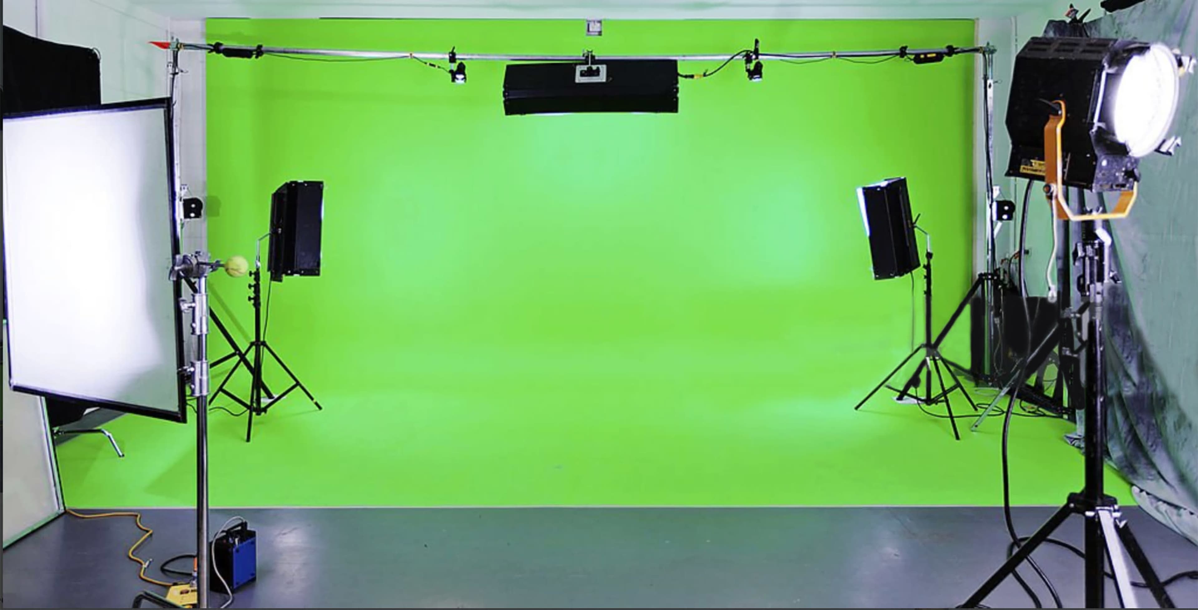 The image shows a green screen studio setup with lighting equipment, including two softbox lights and an overhead light, in a spacious room.