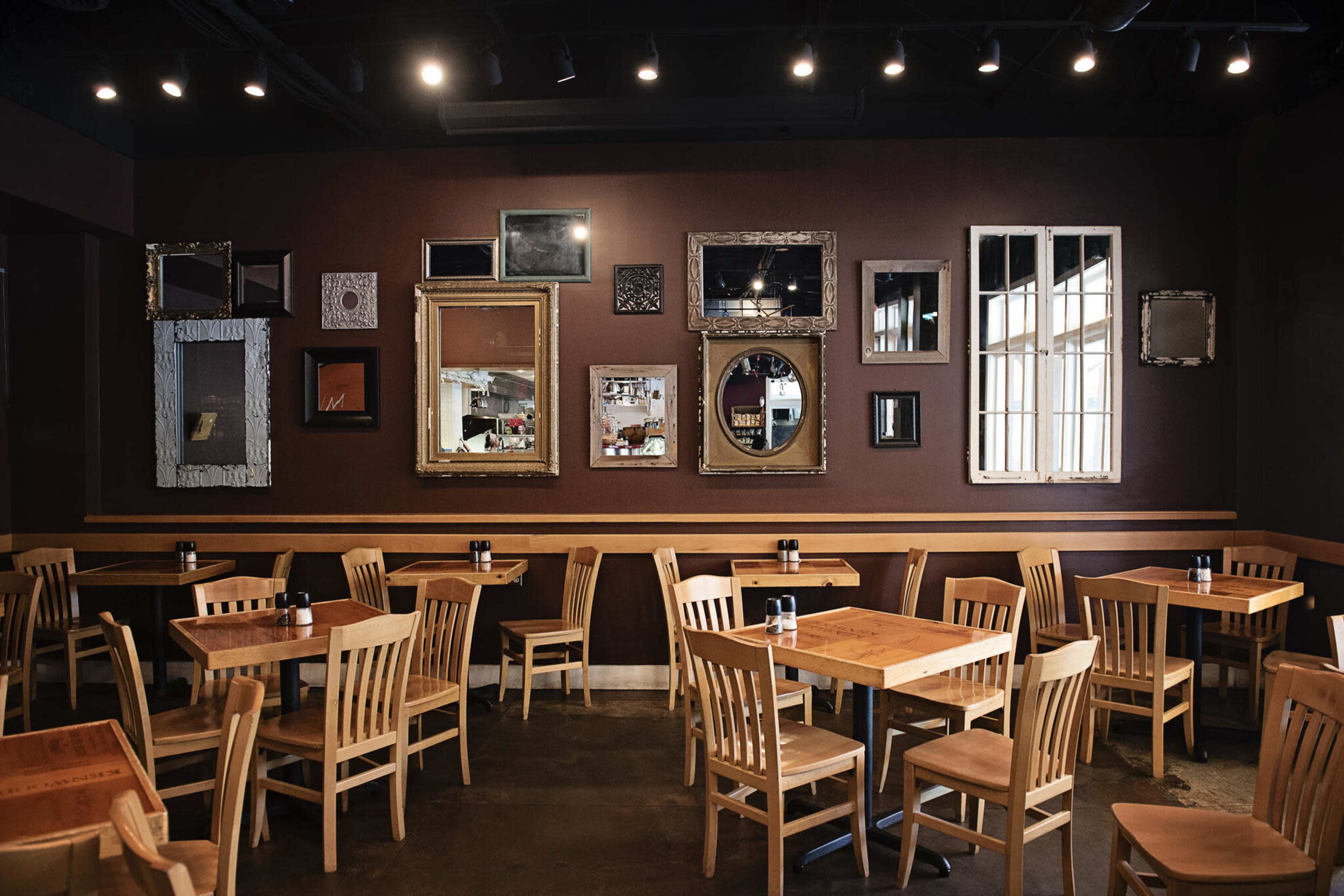 The image shows a cozy restaurant interior with wooden tables and chairs arranged around a wall adorned with various ornate mirrors.