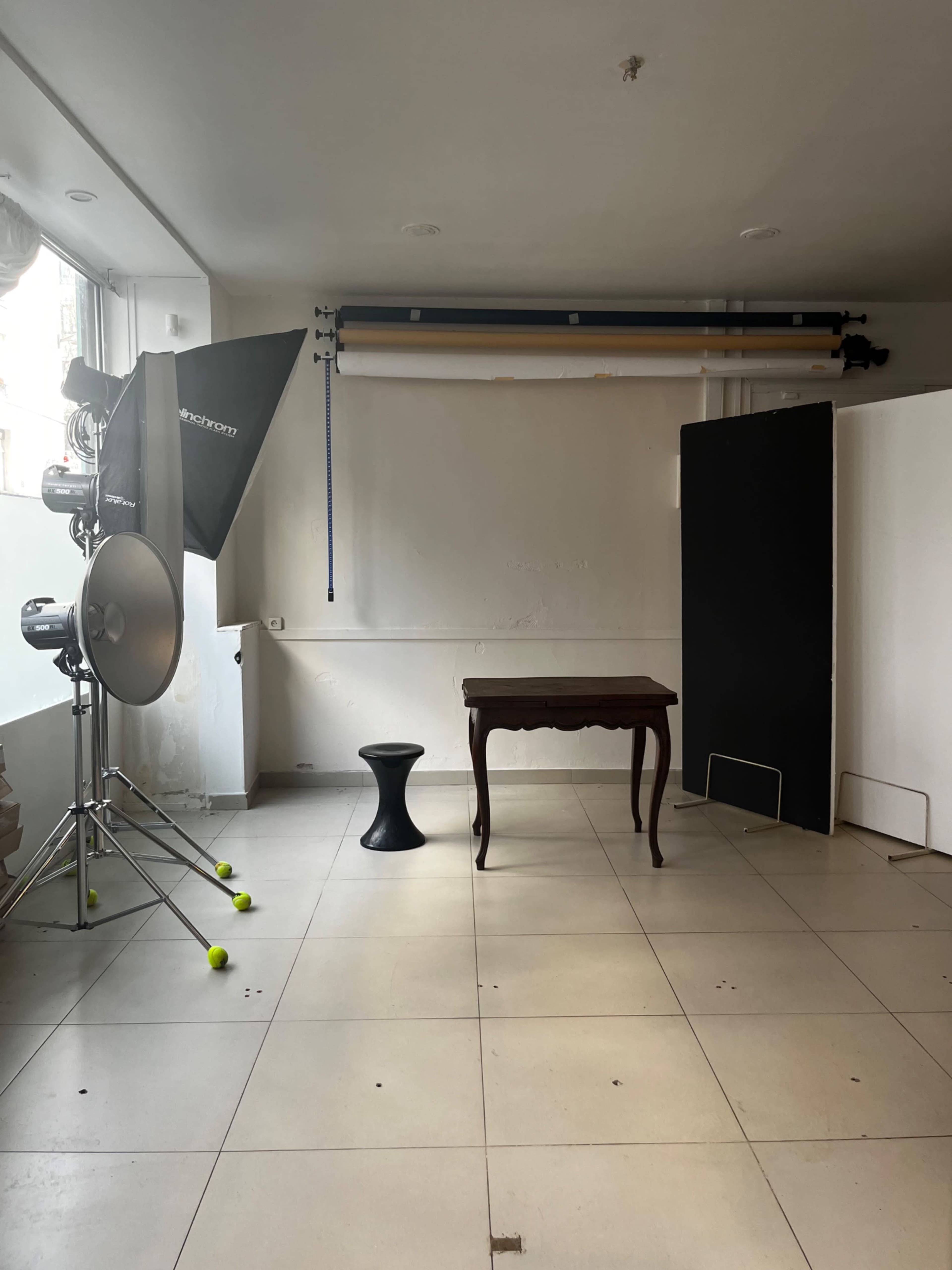 The image shows a photography studio with a light setup, a small table, a stool, and a backdrop.