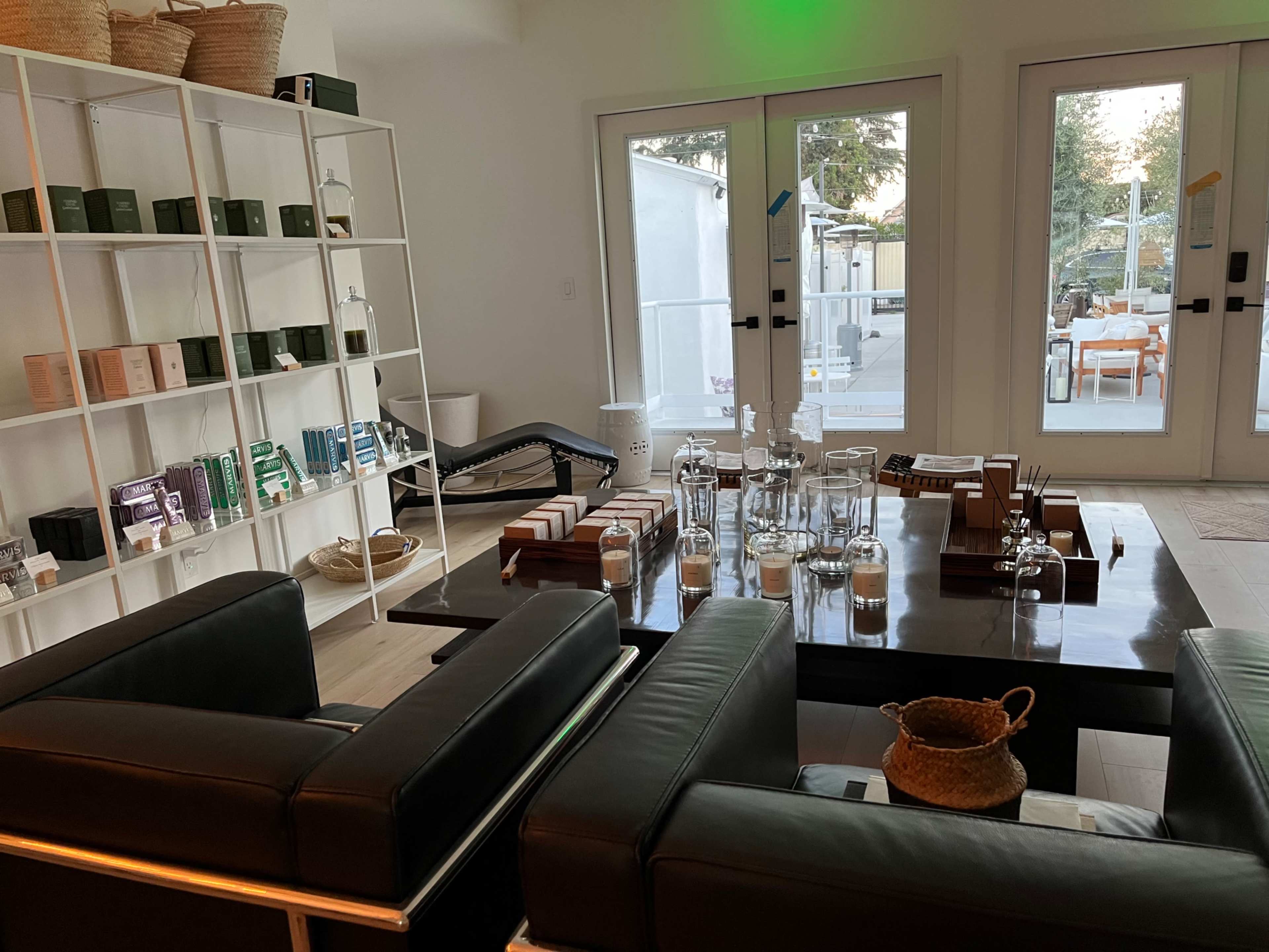 A modern interior space with a black leather seating area, a wooden table set with glassware, and shelves displaying various products.