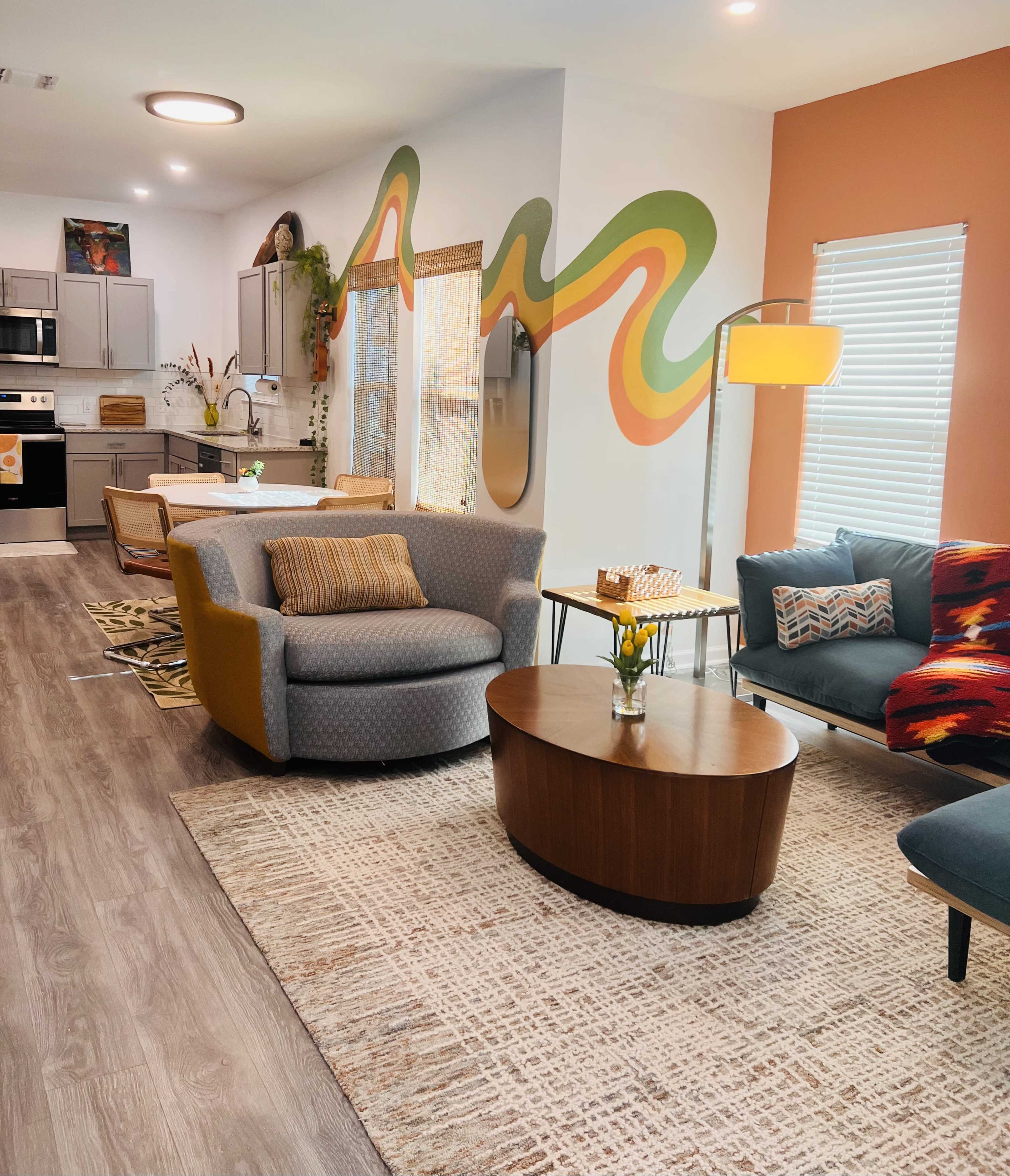 A contemporary living space with a gray and yellow chair, a blue couch, a round coffee table, and colorful wall art, all arranged around a patterned area rug.
