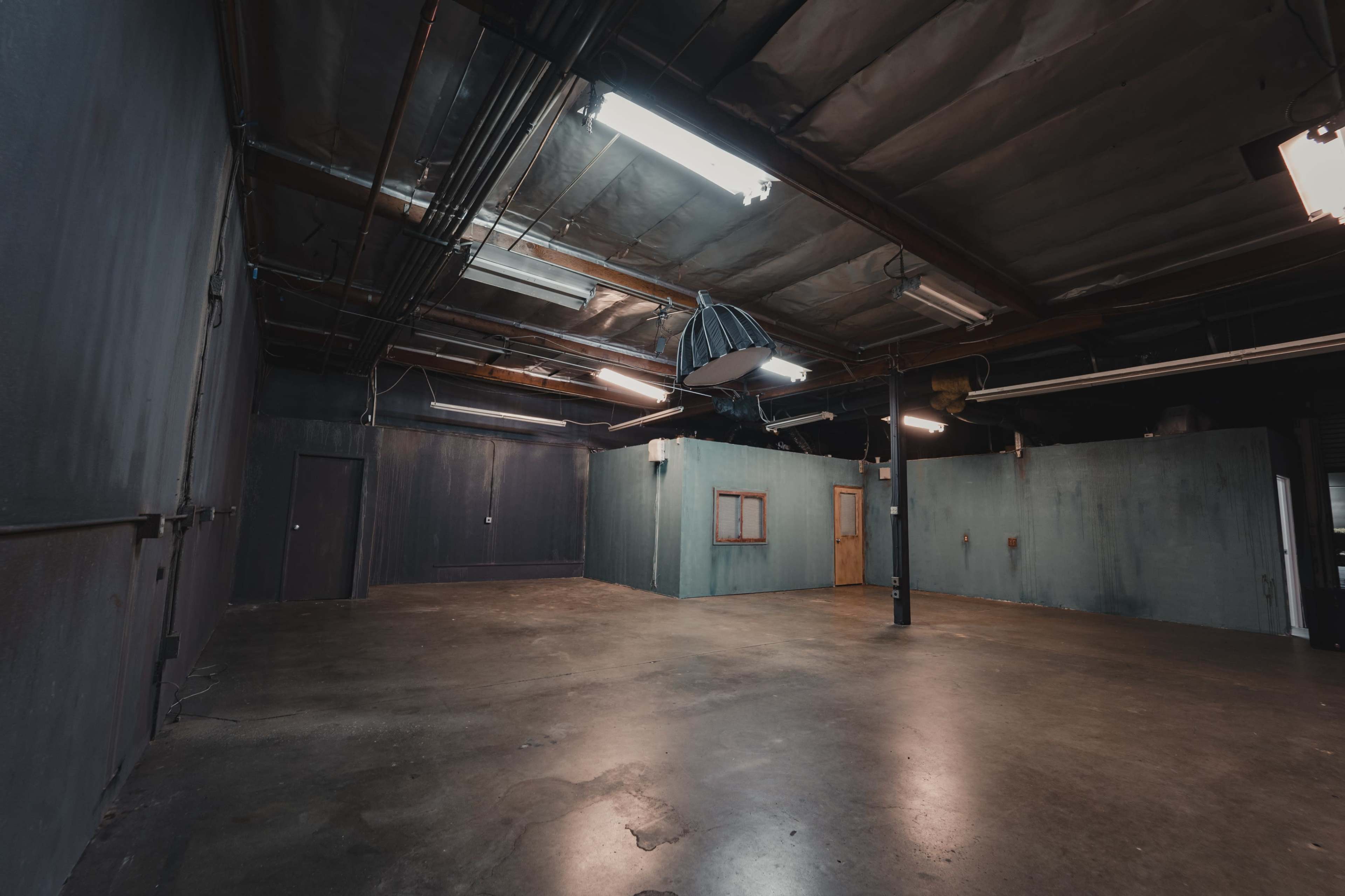 An empty industrial room with bare concrete flooring, dim lighting, and walls painted in dark colors.