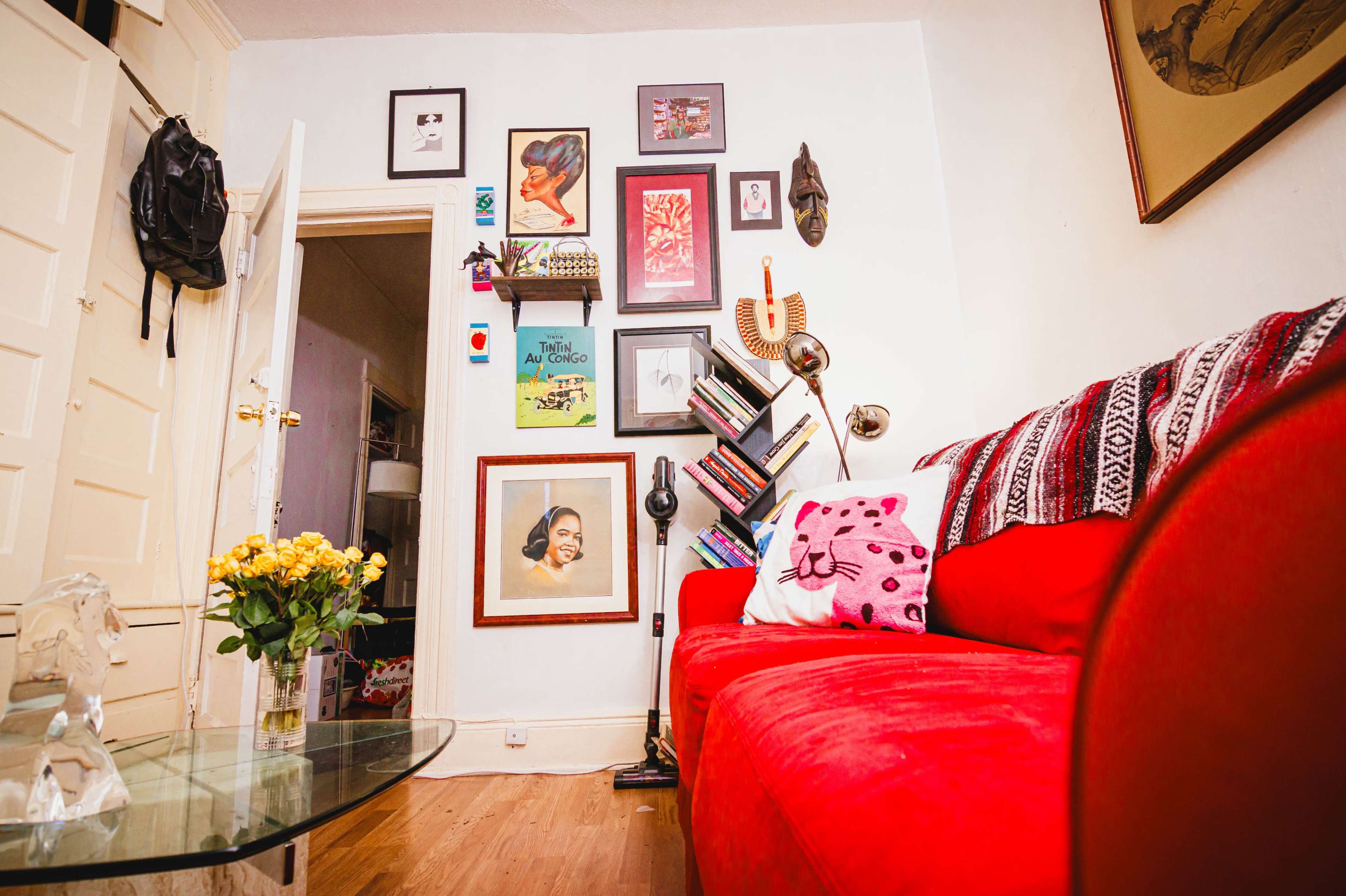 A red sofa is positioned in a cozy living room adorned with framed artwork and a bookshelf.