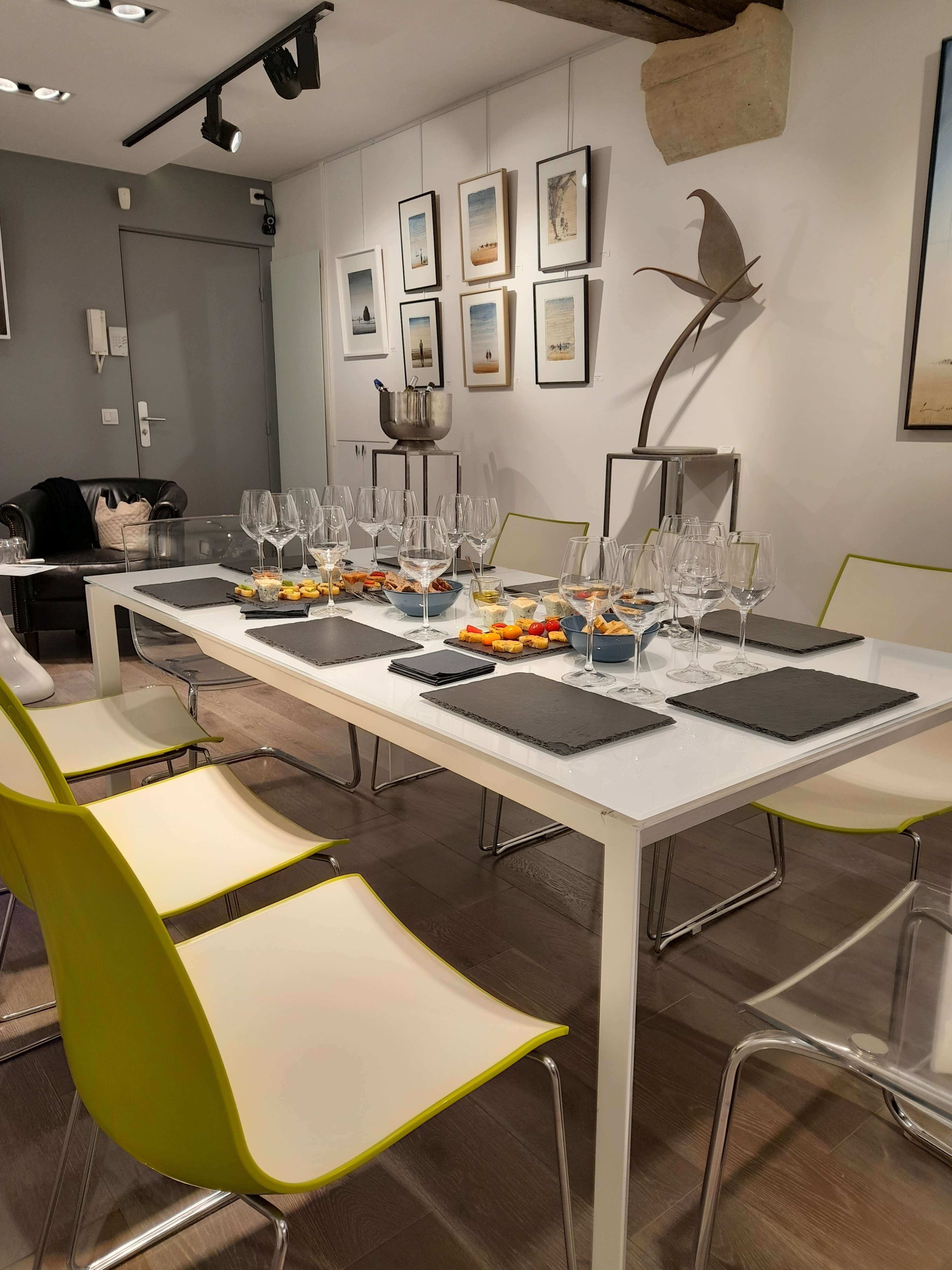 A dining table set with glasses and snacks is surrounded by modern chairs in a well-lit room adorned with framed images on the walls.