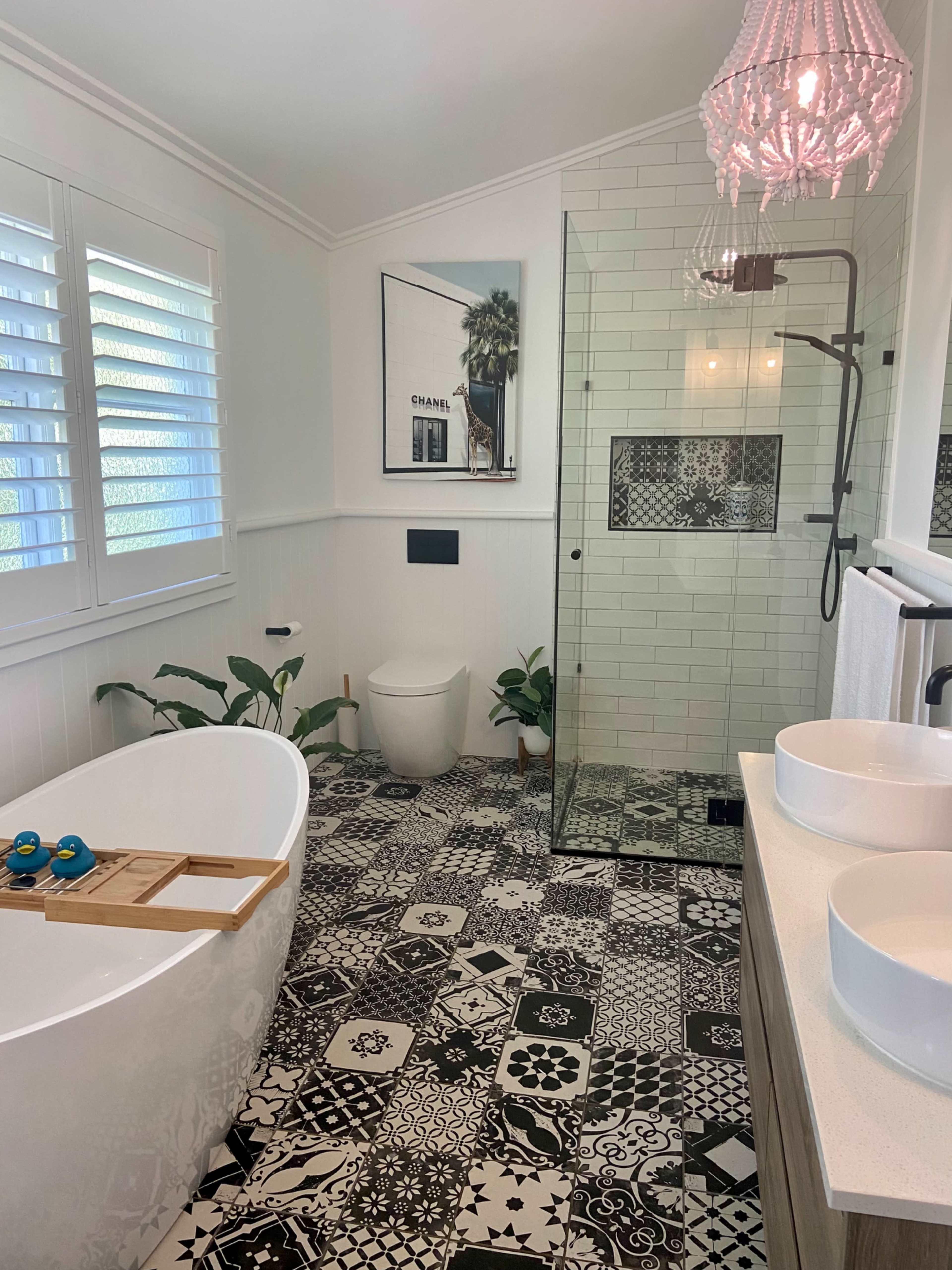 A modern bathroom features a freestanding bathtub, a walk-in shower with glass walls, patterned tile flooring, and greenery accents.