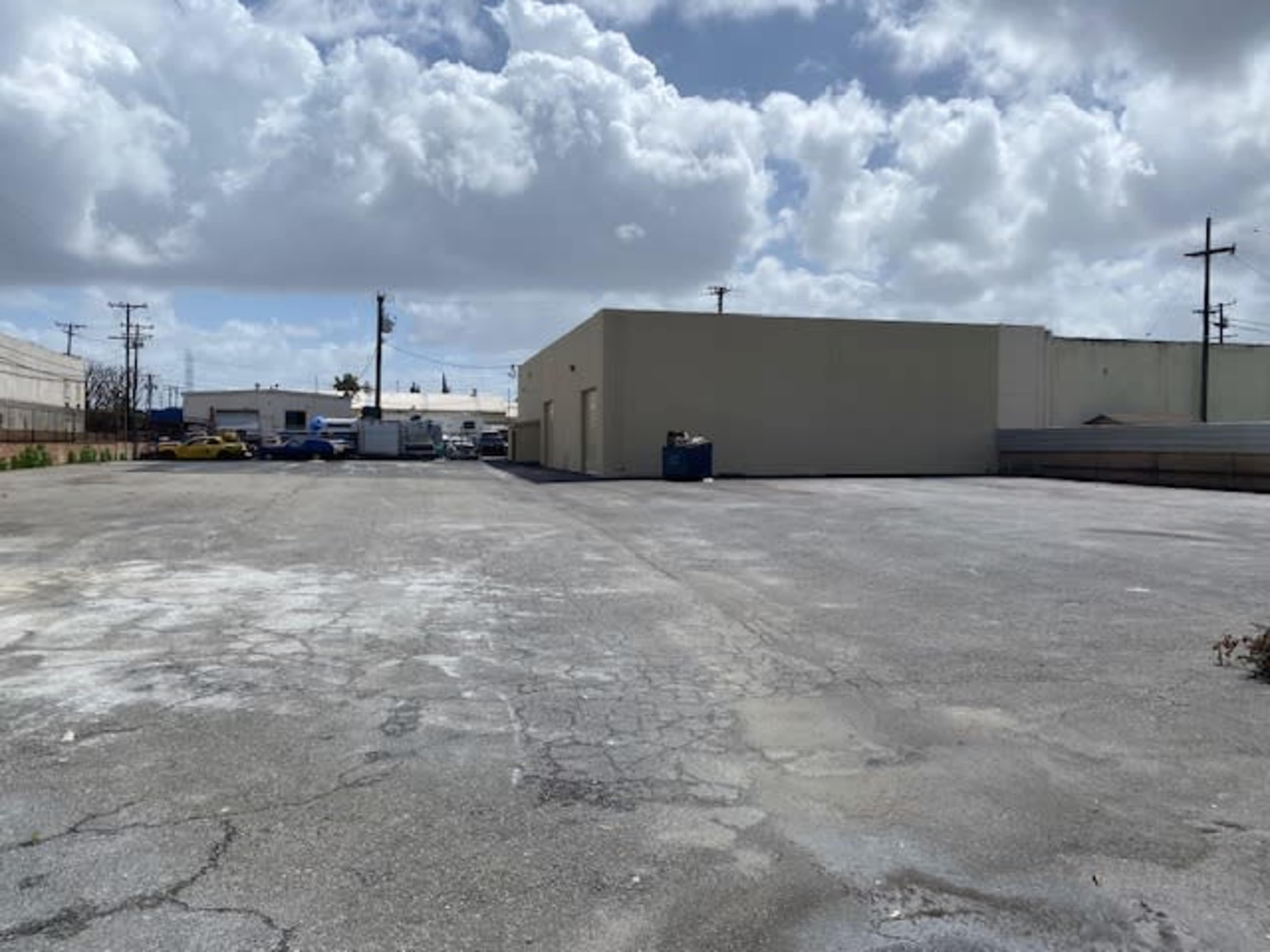 A deserted parking lot with cracked pavement, surrounded by buildings under a cloudy sky.