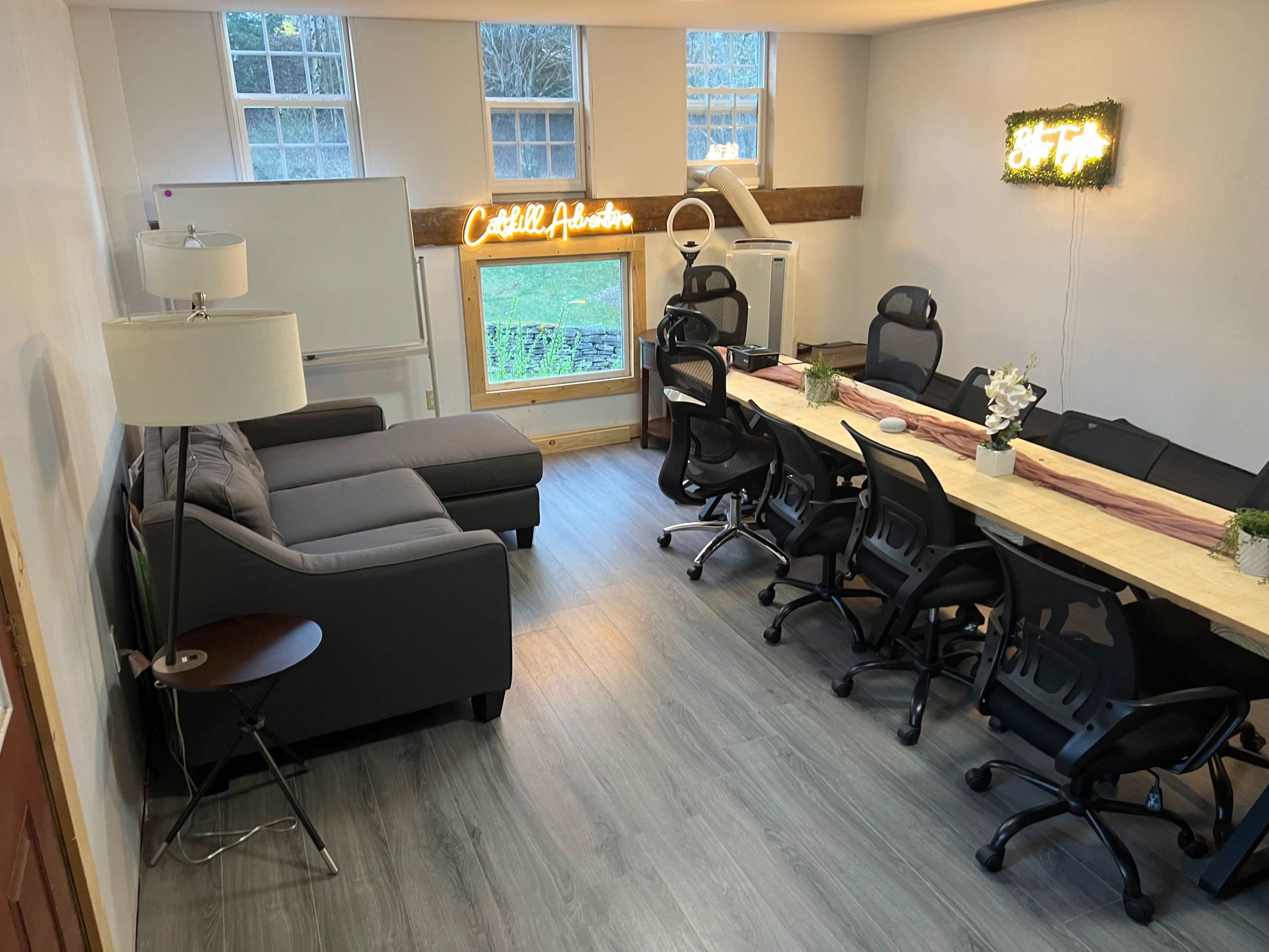 A modern meeting room with a long table, multiple office chairs, a gray sectional sofa, and windows allowing natural light.