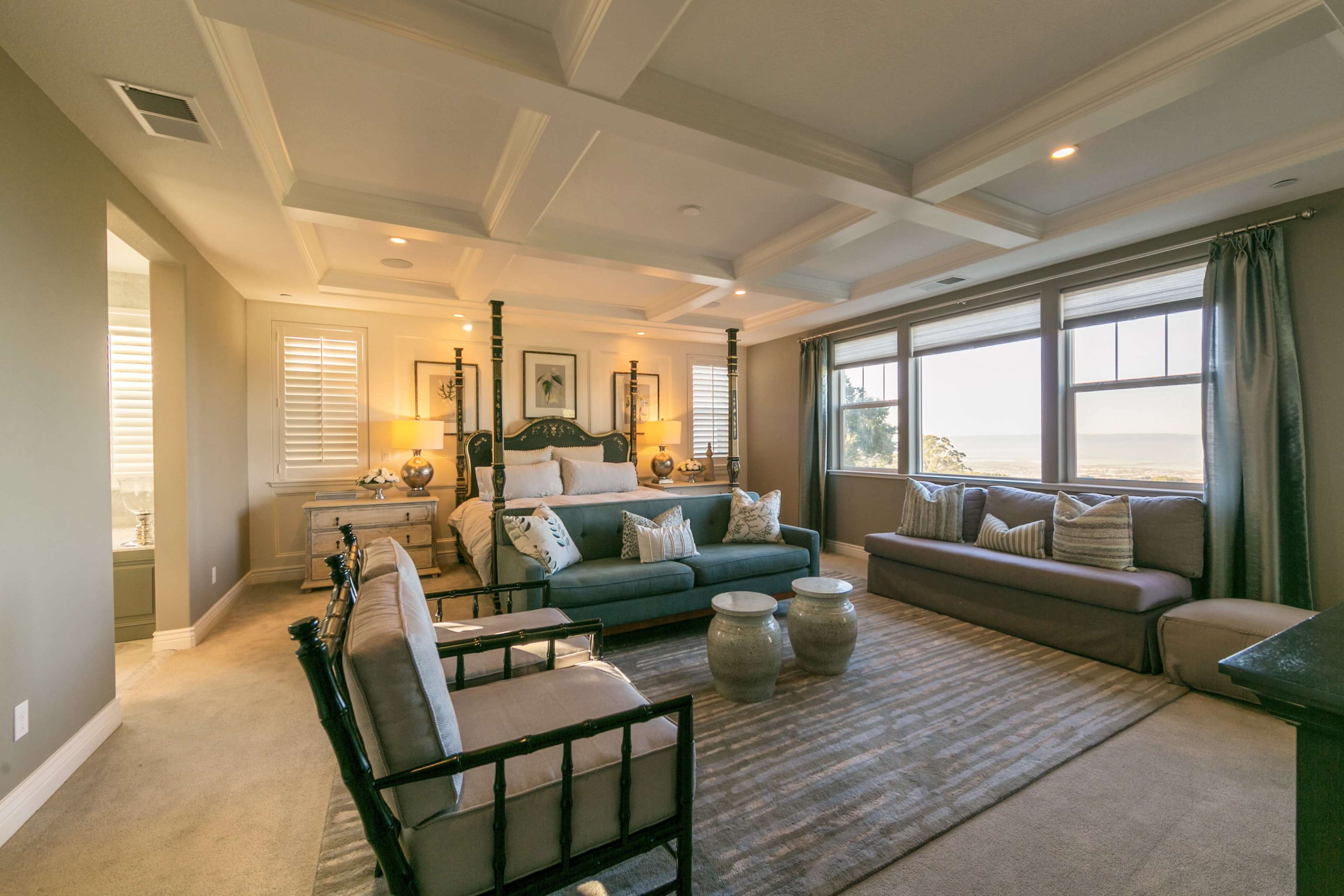 A well-furnished bedroom featuring a bed, seating area, and large windows with a view of the ocean.