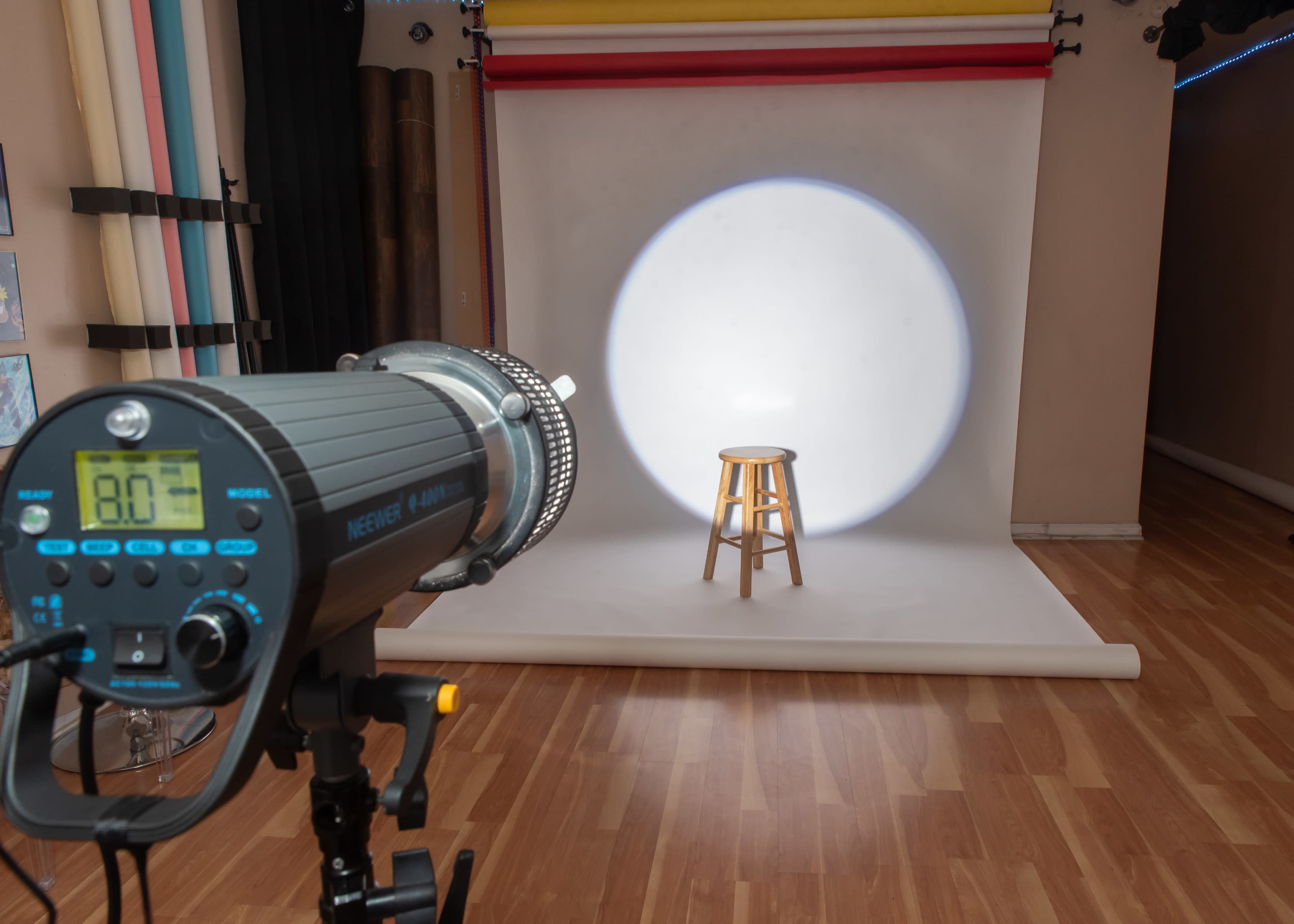 A spotlight is focused on a wooden stool in a photography studio with colorful backdrops.