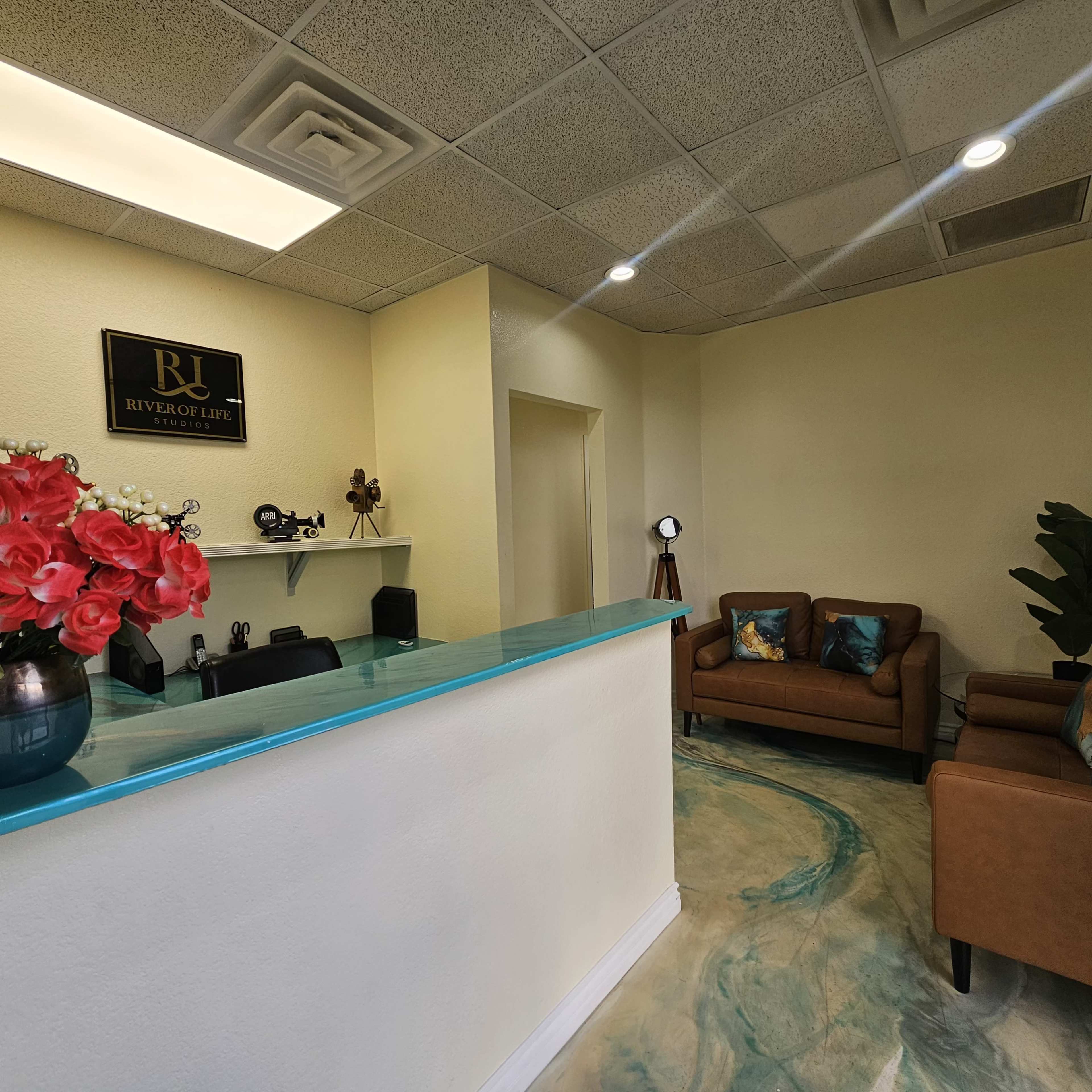 The image shows a reception area with a turquoise front desk, brown leather seating, a plant, and decorative items.