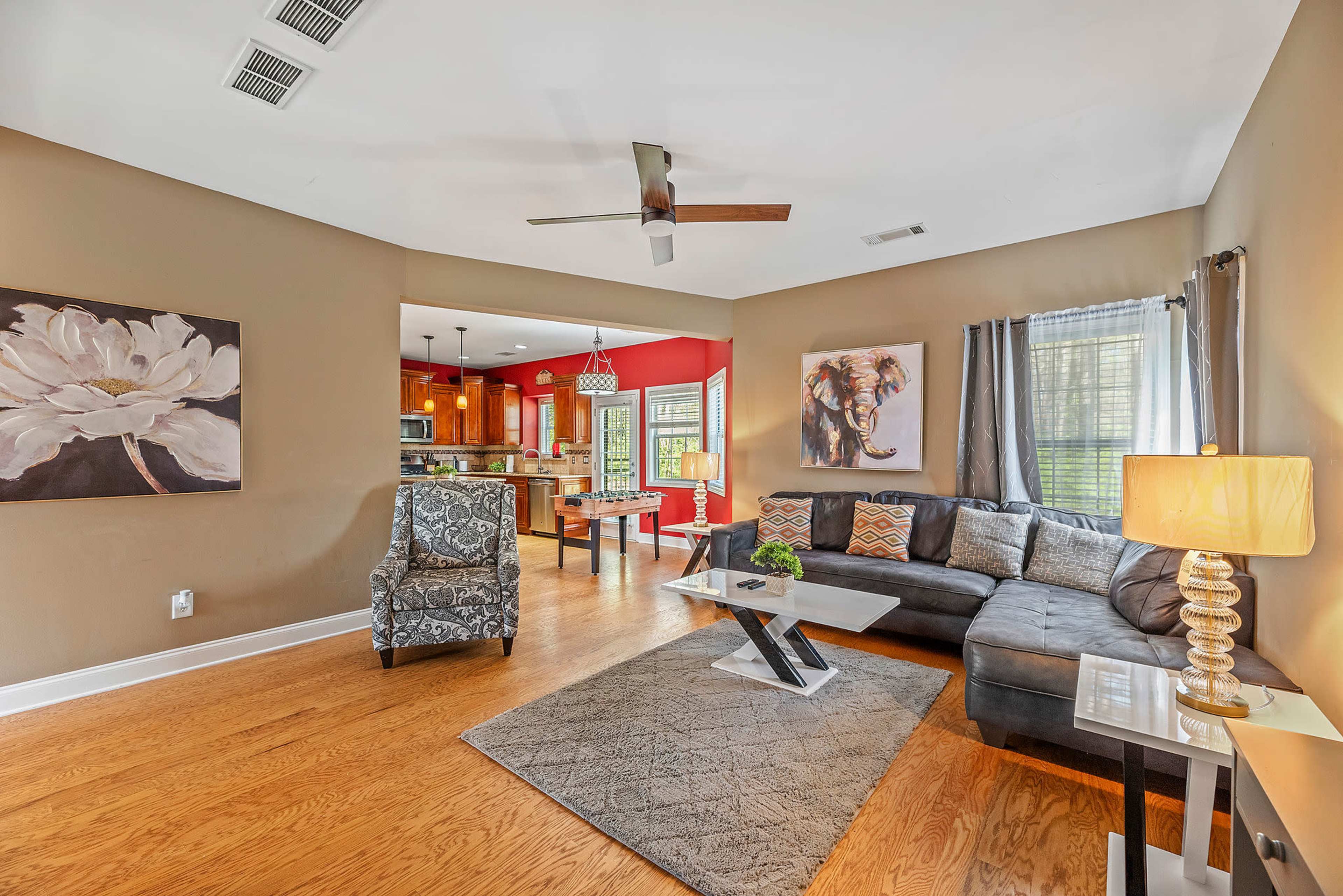A spacious living room with a modern sectional sofa, a decorative chair, and a coffee table, leading into a kitchen with red walls and wood cabinetry.