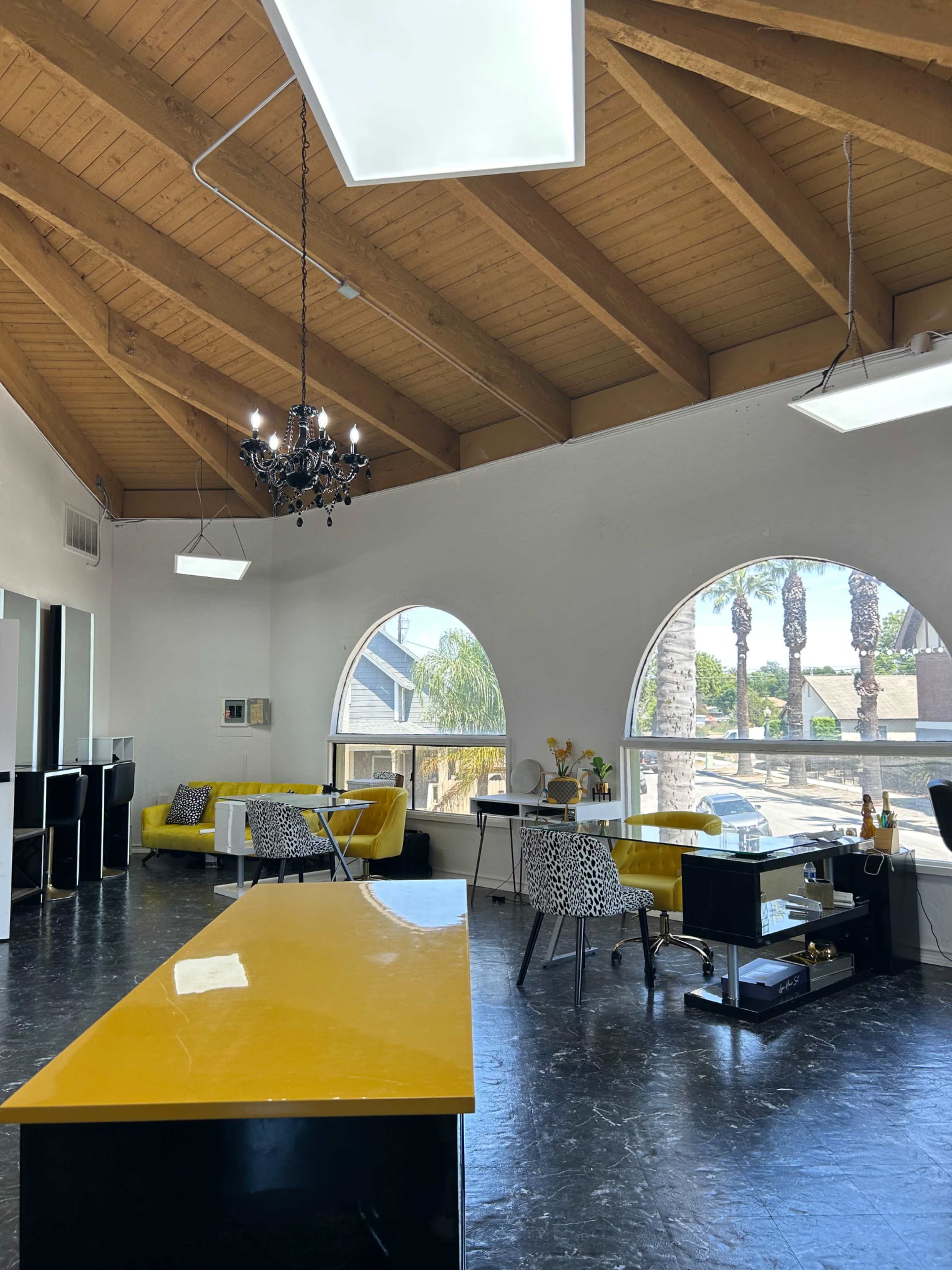 A spacious room with a modern design, featuring a yellow countertop, arched windows, and a mix of seating arrangements, including a yellow sofa and patterned chairs.