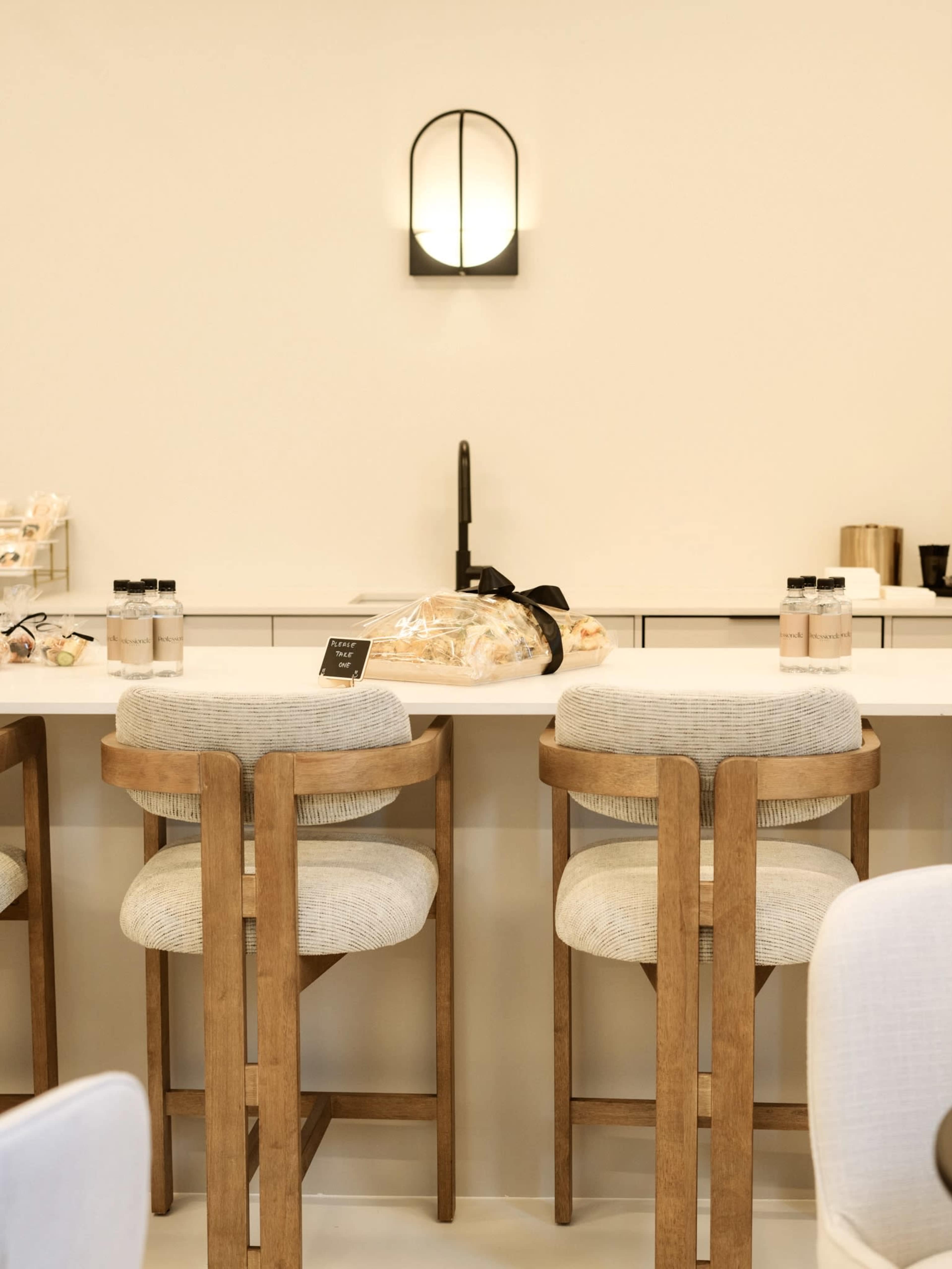 A minimalist kitchen features a light-colored countertop with two wooden stools and a wall-mounted light fixture.