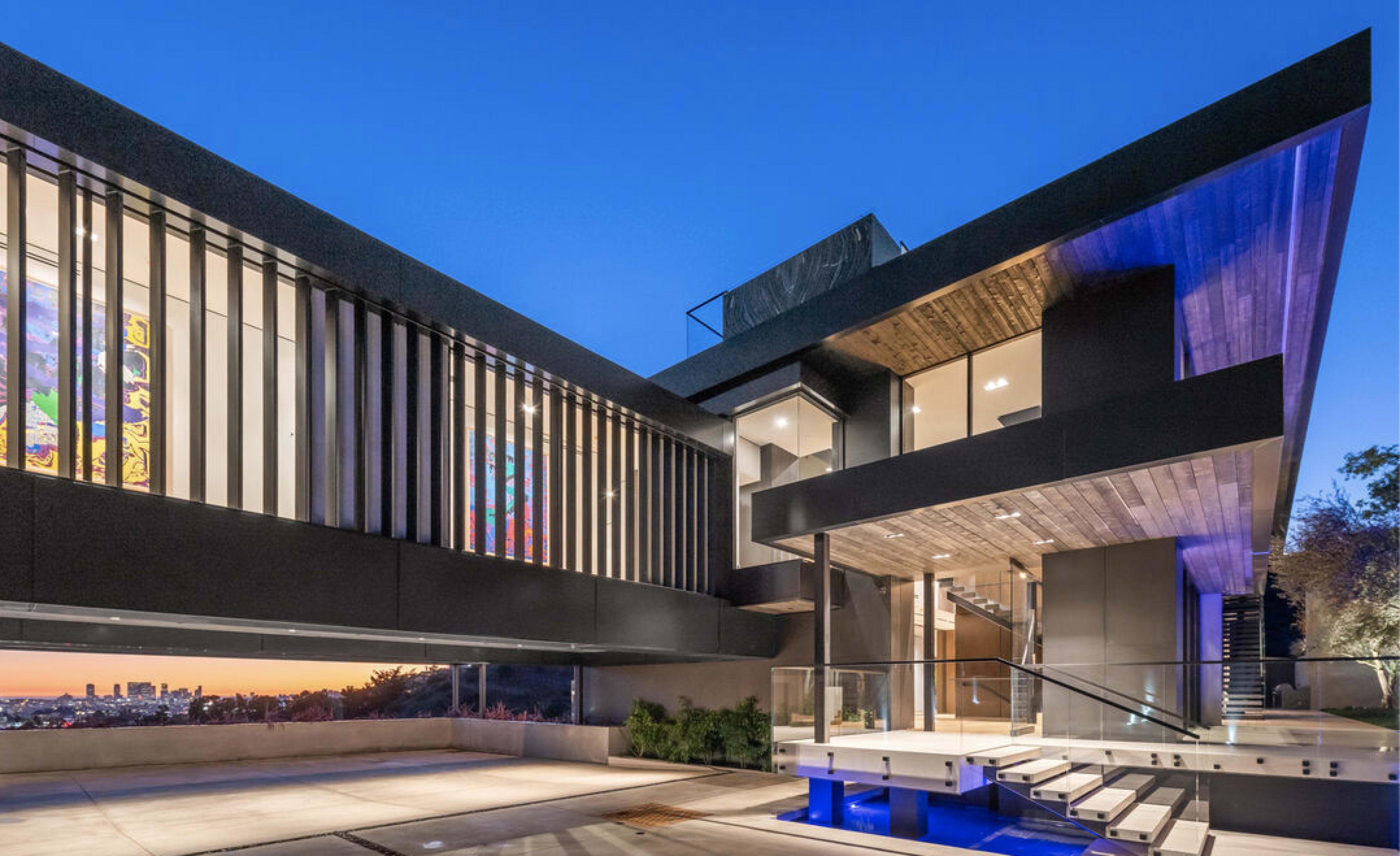 A modern, multi-level house features large windows and a sleek, angular design, set against a twilight sky.