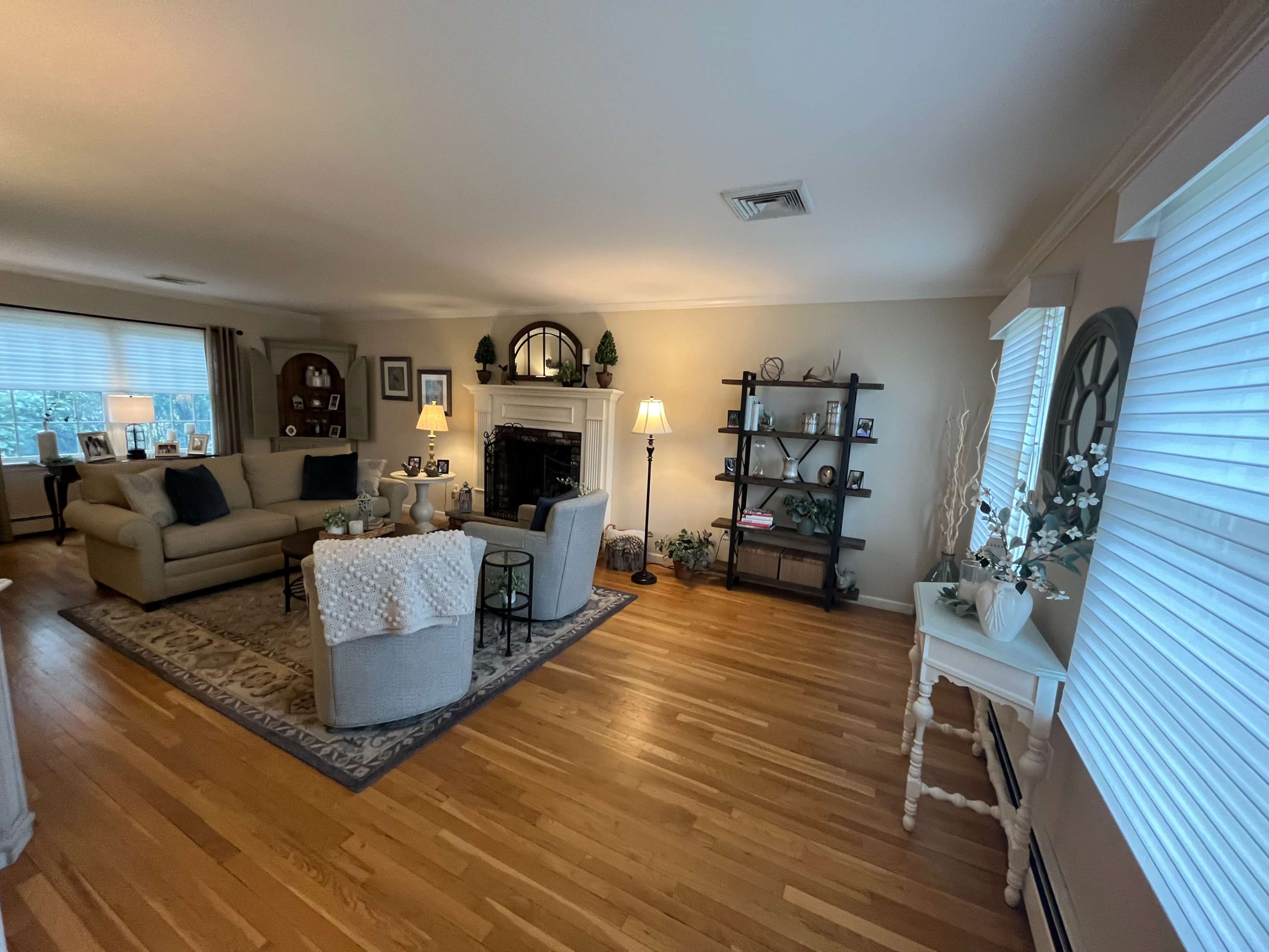 A living room with a beige sofa, a comfortable chair, a fireplace, shelves with decorative items, and large windows letting in natural light.
