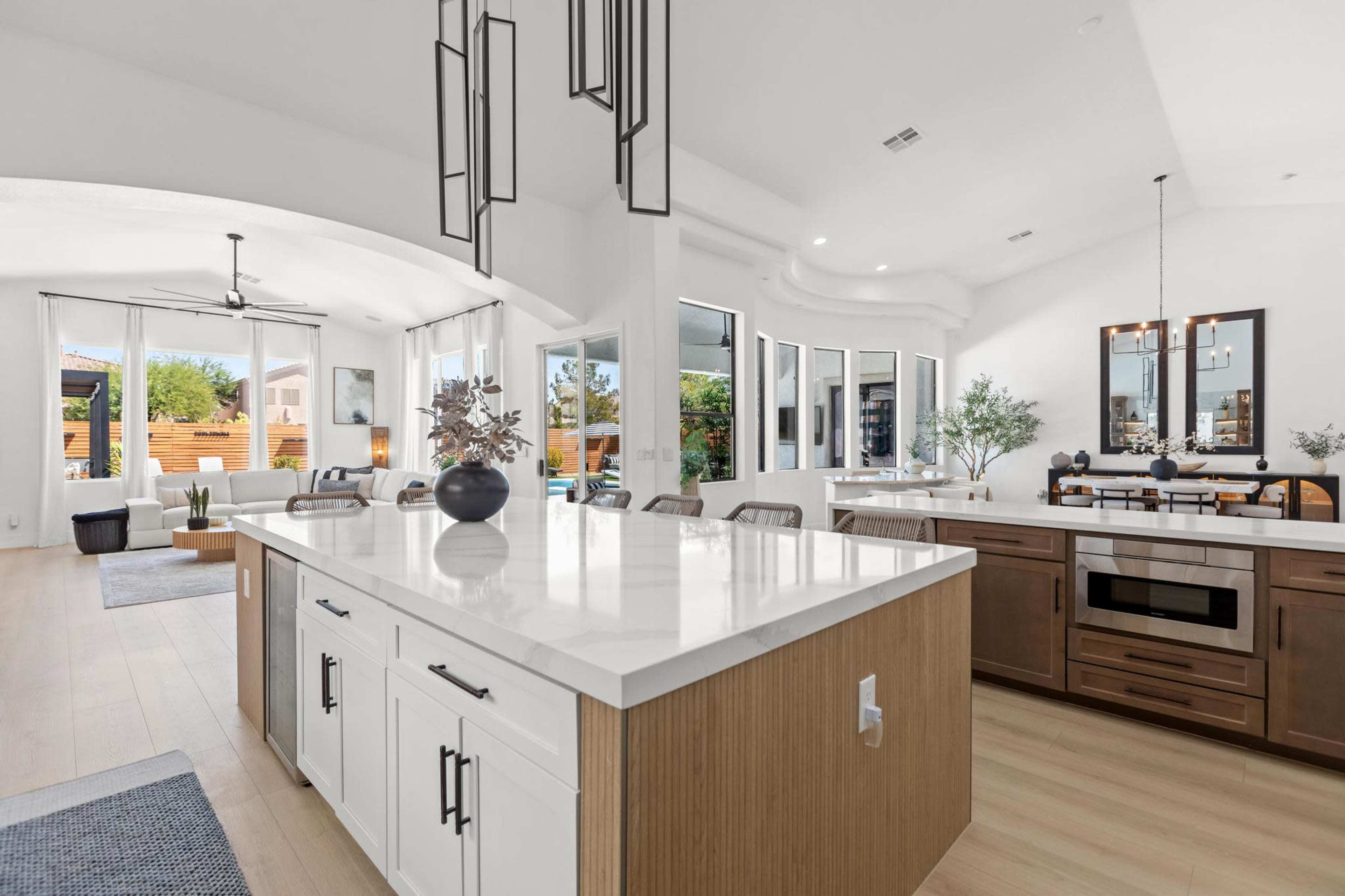 The image shows a modern kitchen with an island, pendant lights, and large windows that provide natural light.