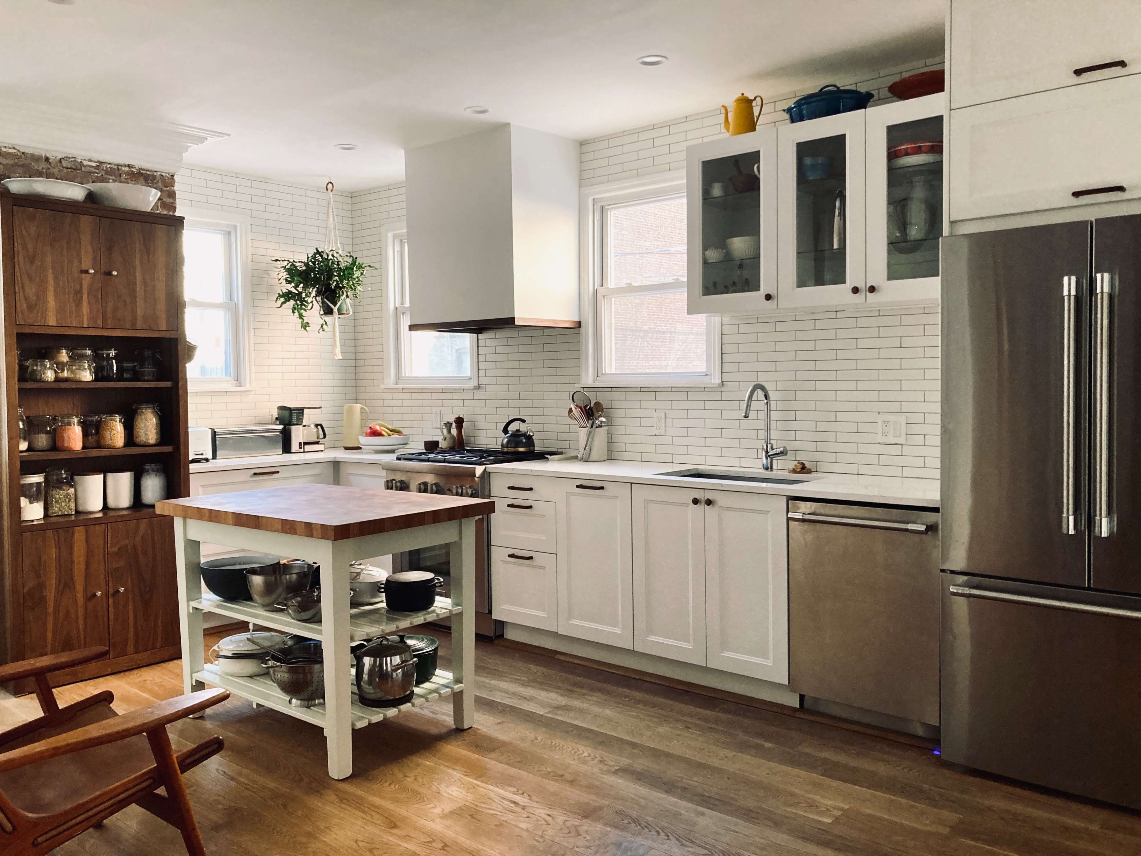 A modern kitchen with white cabinetry, a wooden island with a butcher block top, and stainless steel appliances.