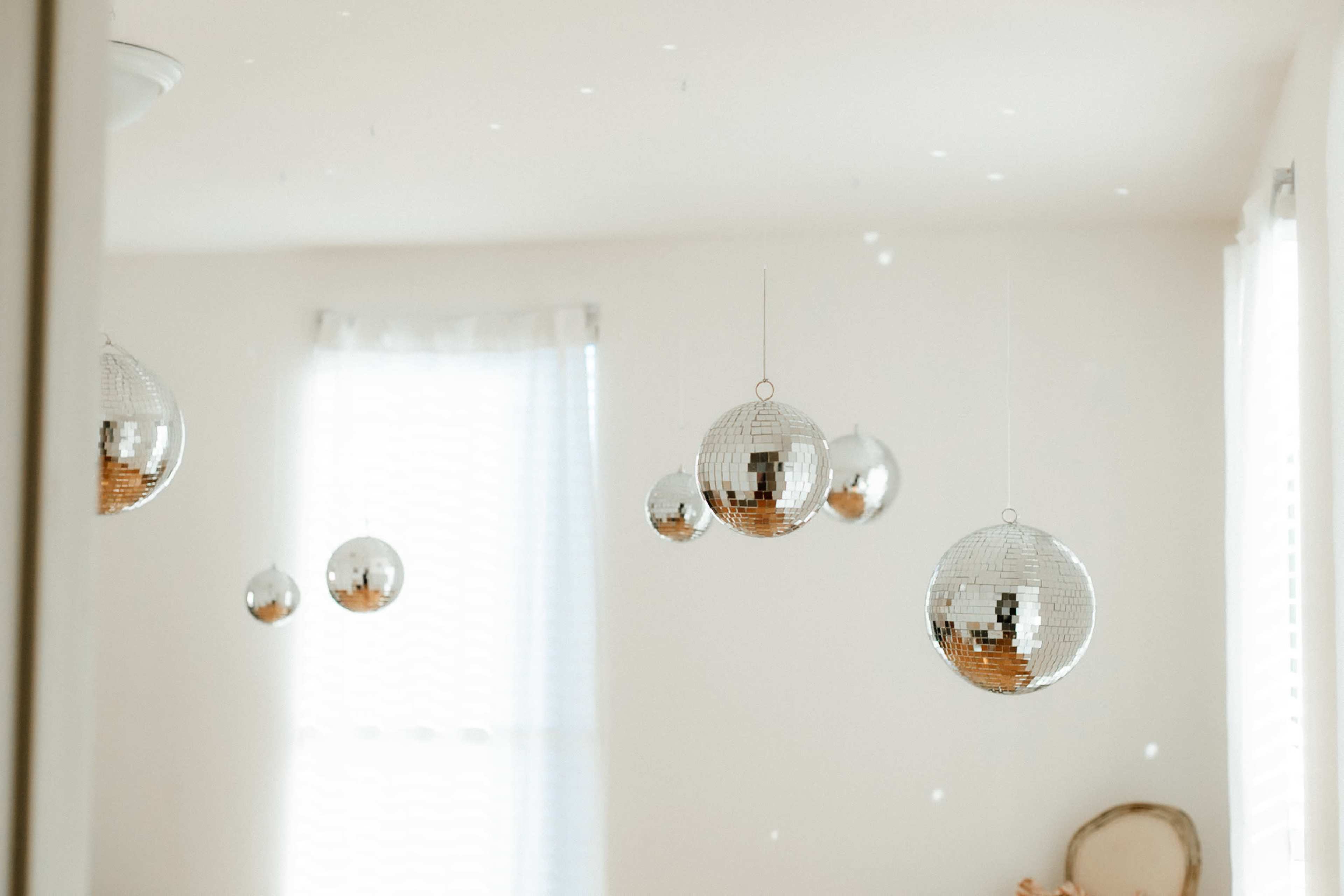 Several hanging disco balls reflecting light in a room with white walls and a window.