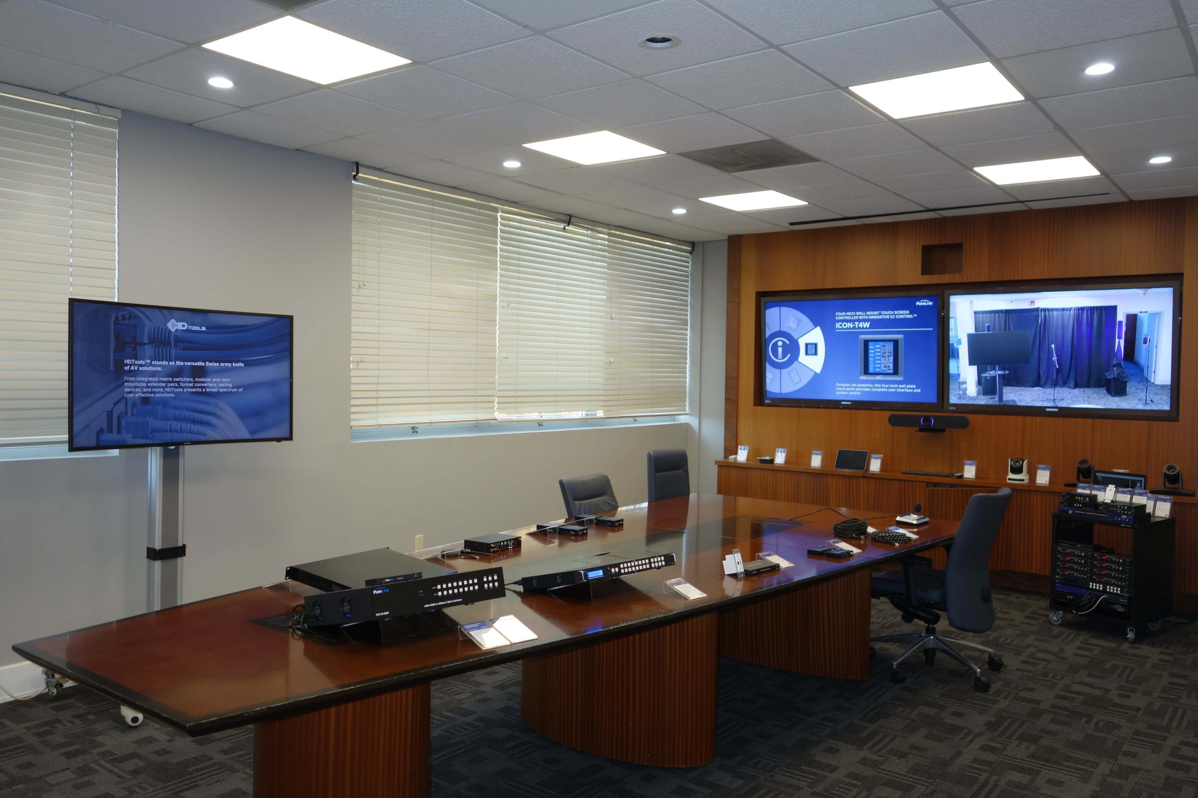 A modern conference room equipped with a large table, multiple screens, and a variety of audio-visual equipment.