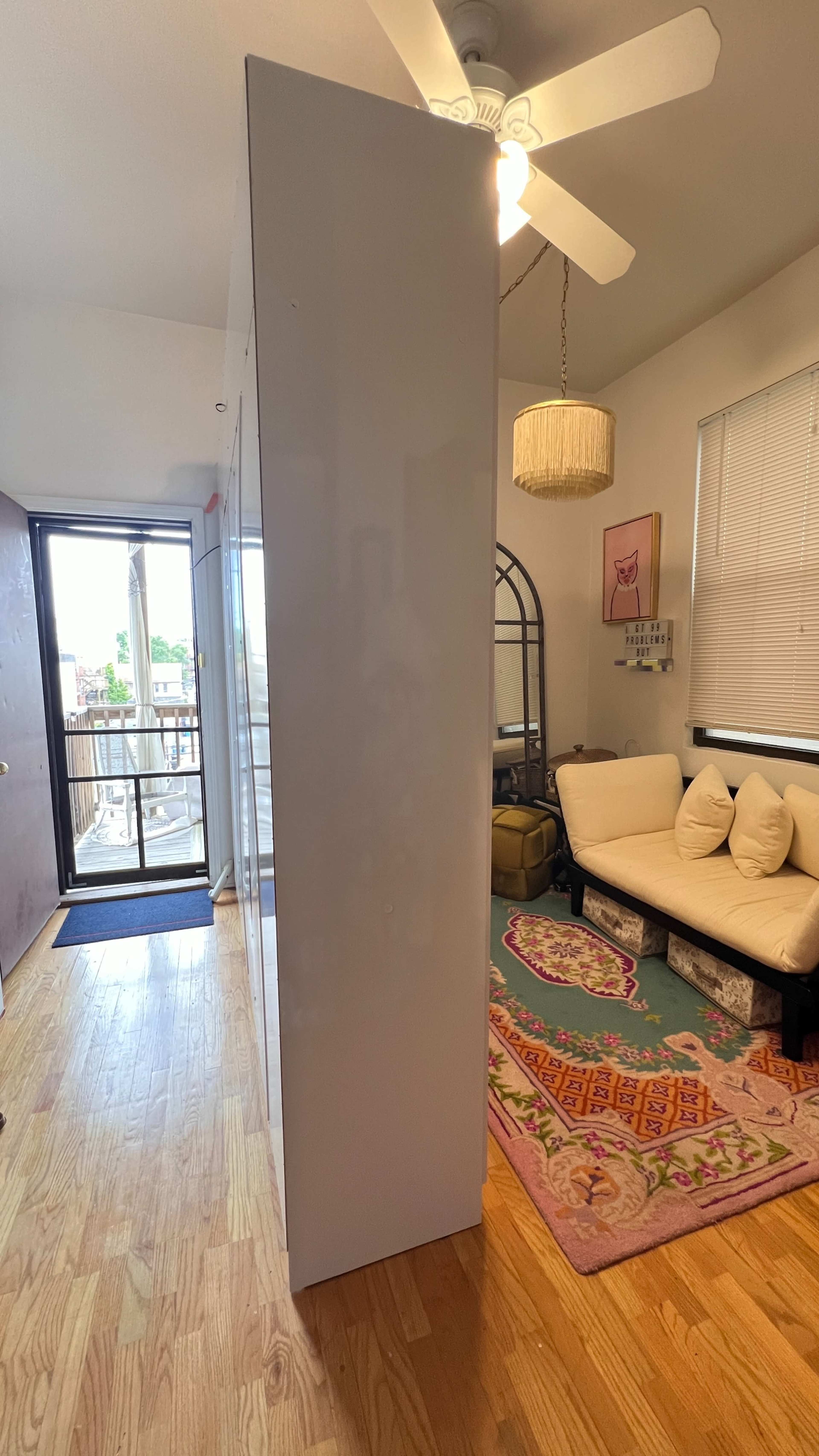 A narrow white partition dividing a room that includes a couch, decorative rug, and access to a balcony through a glass door.