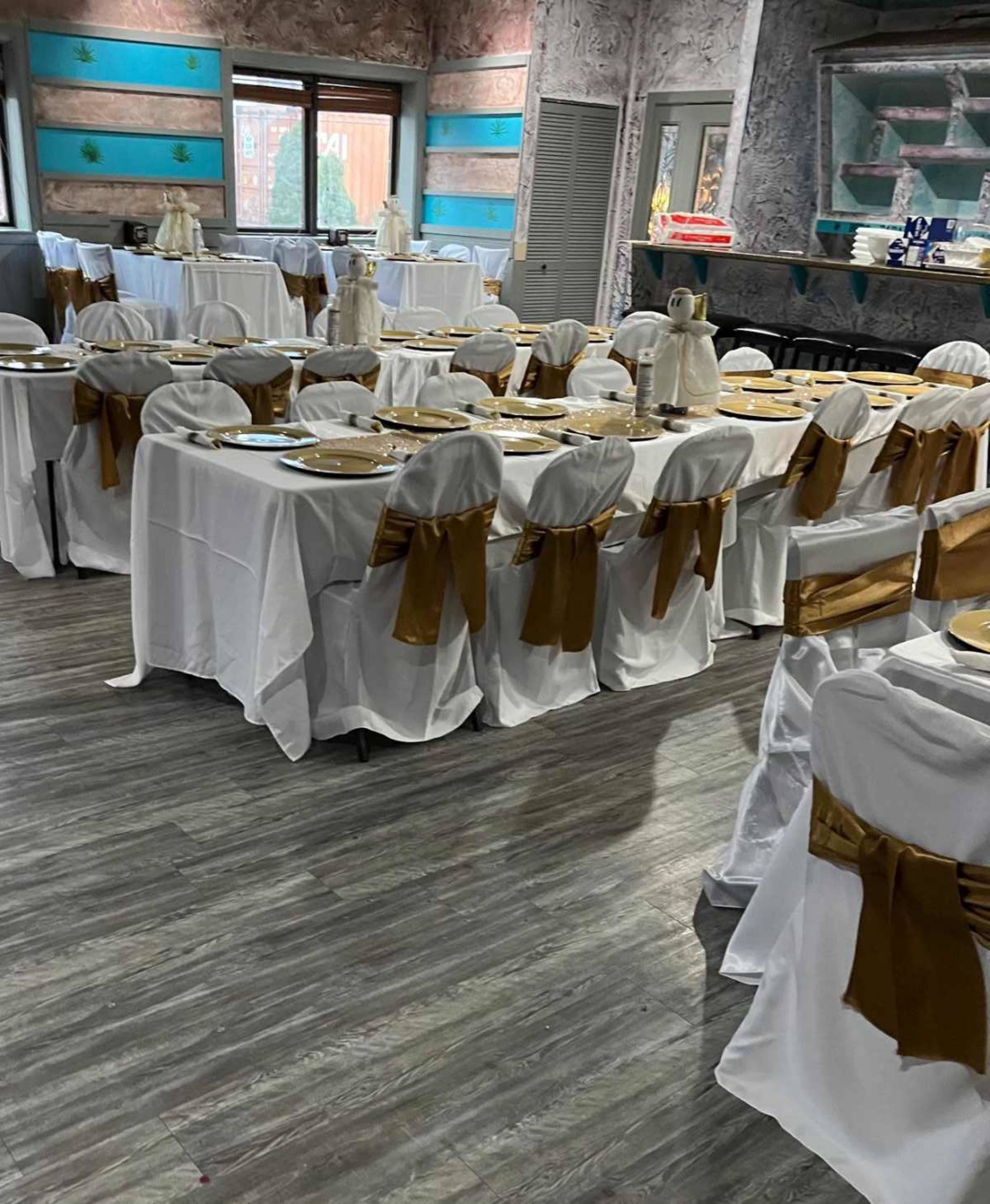 A banquet hall set up with multiple tables covered in white tablecloths and adorned with gold chair sashes.