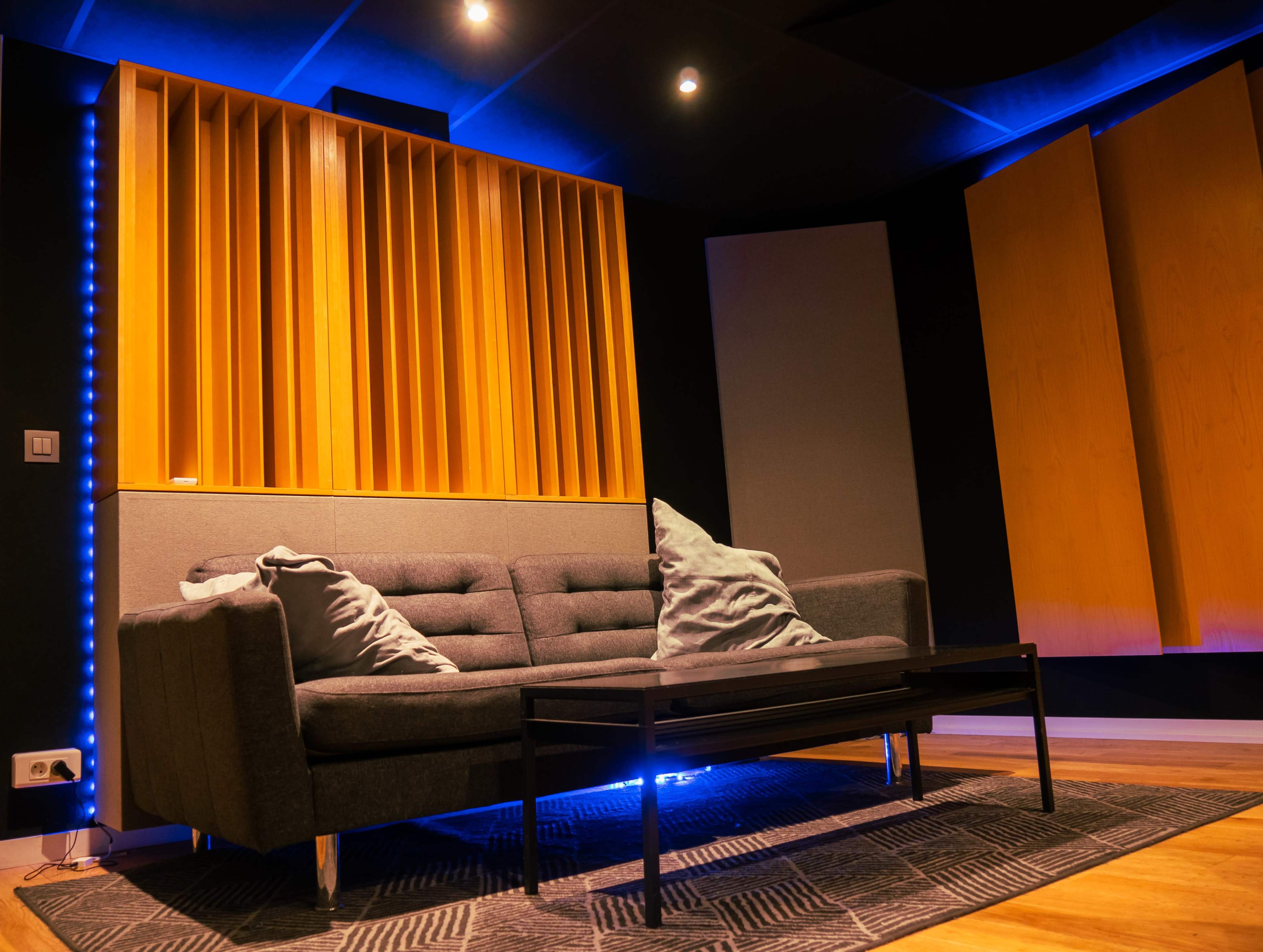 A modern sound studio with a gray sofa, a black coffee table, and wooden acoustic panels on the walls.