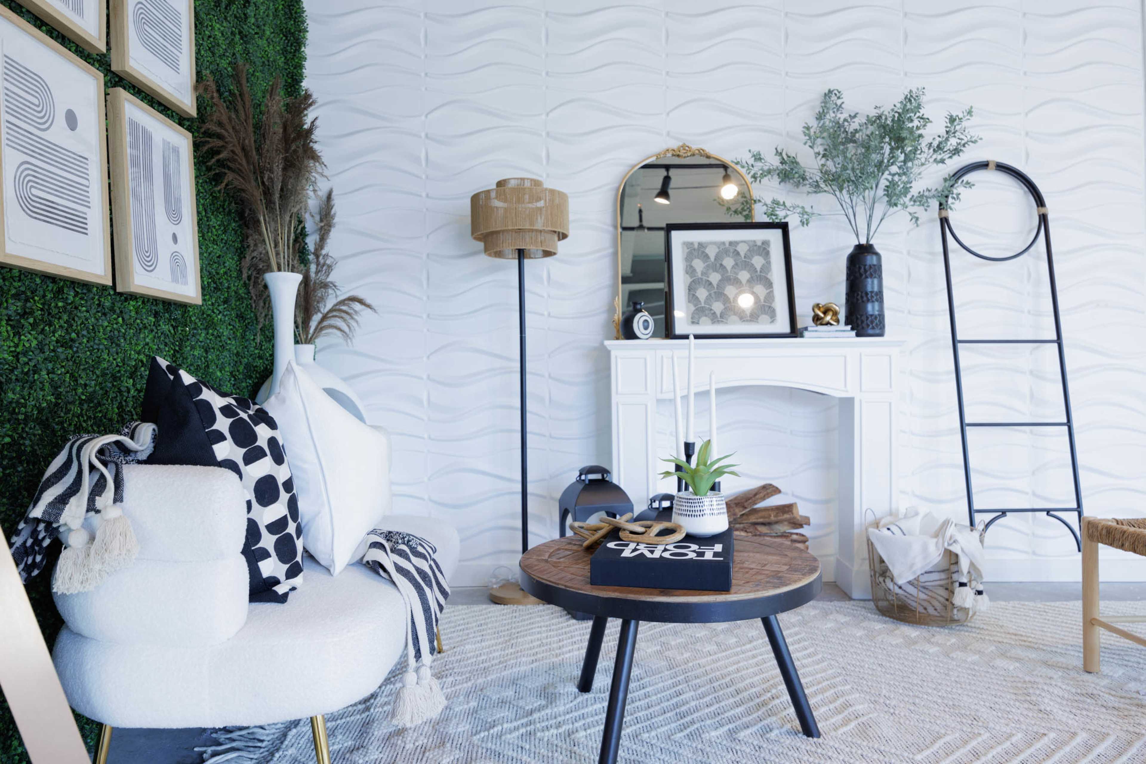 The image depicts a modern living room featuring a white textured wall, a round wooden coffee table, a cozy white armchair, and various decorative plants and artwork.