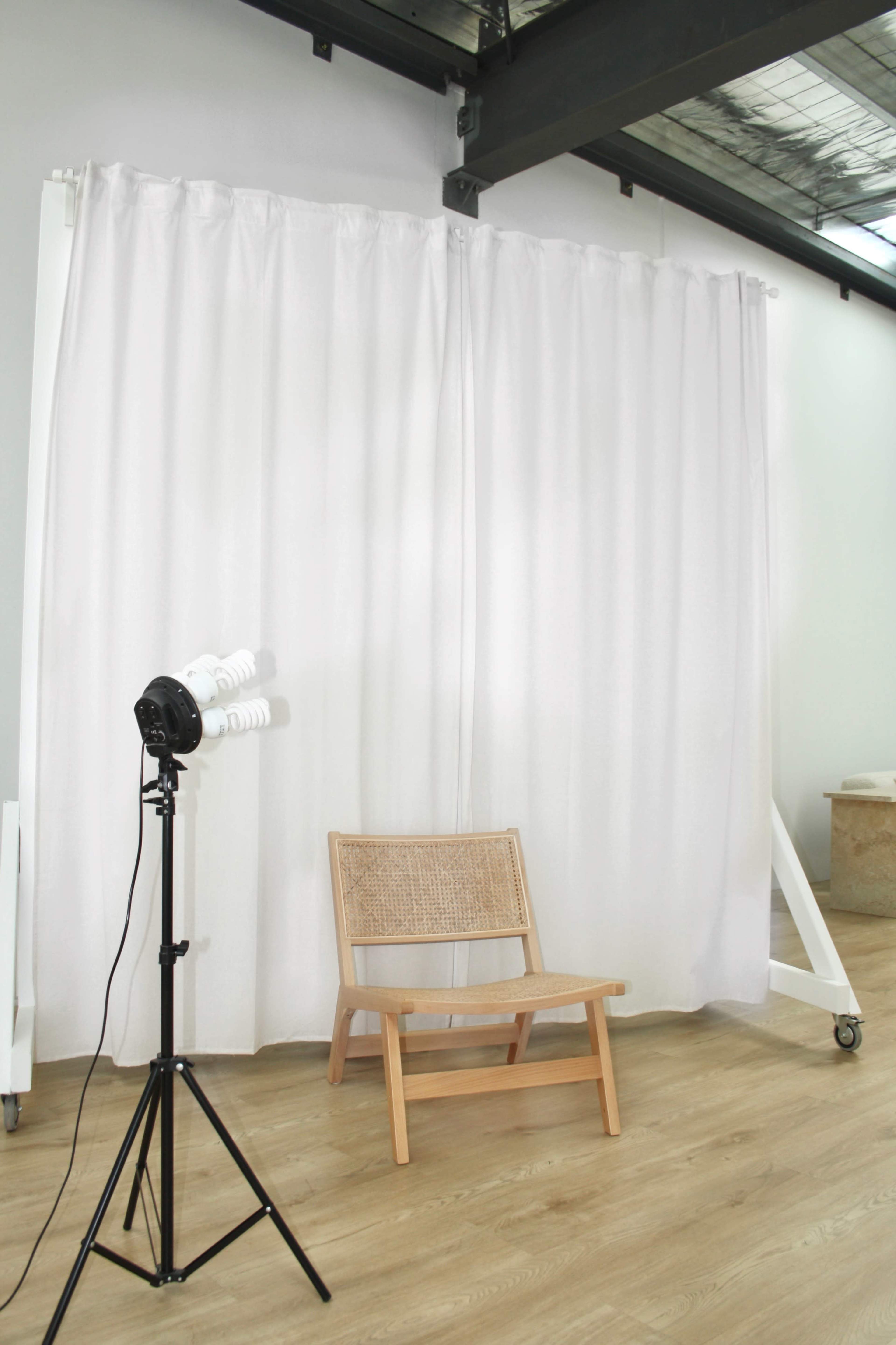 A white curtain drapes across a partitioned area with a wooden chair and a lighting equipment stand beside it.
